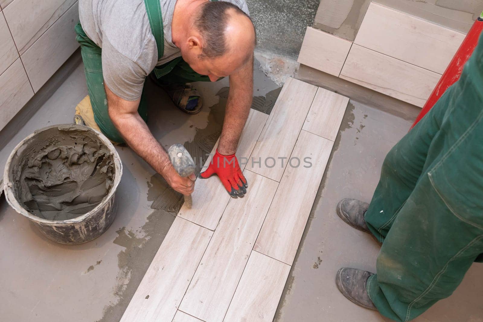 Rubber hammer. An experienced construction worker. Laying terracotta in the bathroom. Work clothes. He knocks with a hammer.