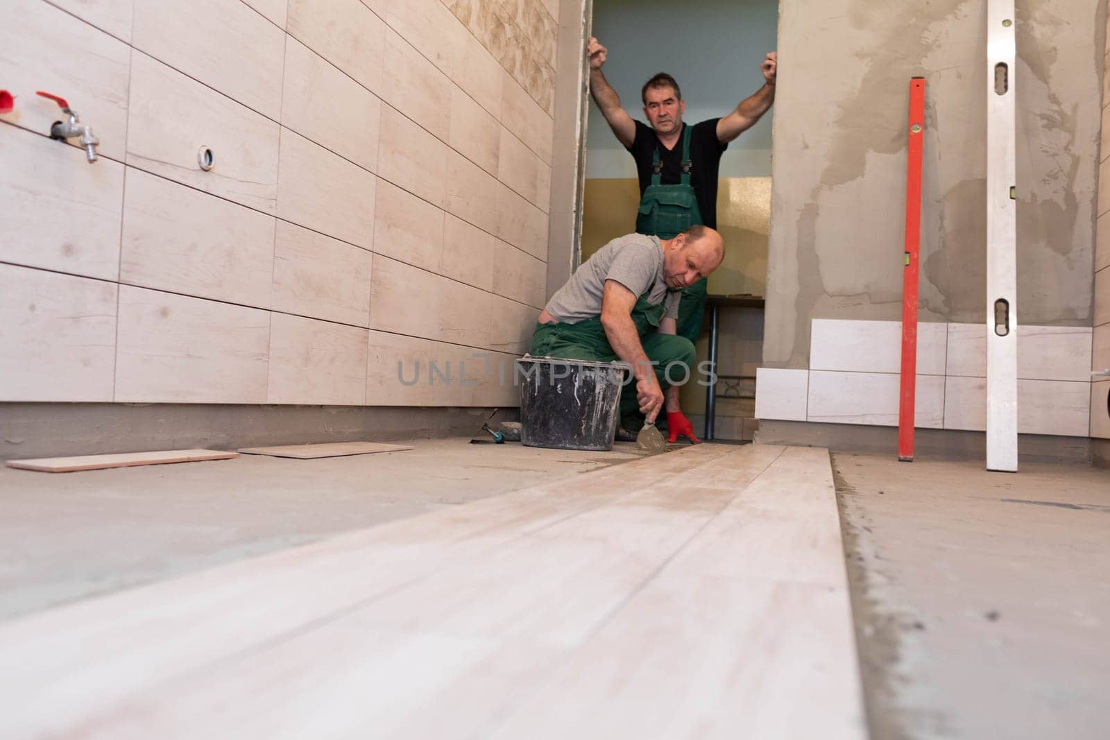 Professional construction worker laying ceramic tiles on the floor in the bathroom room.