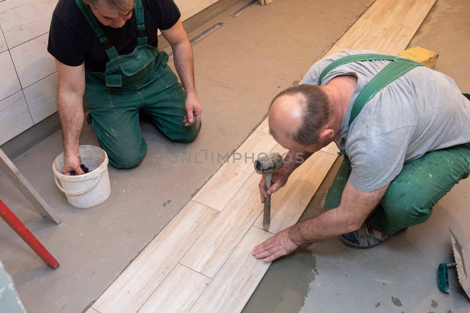 Rubber hammer. An experienced construction worker. Laying terracotta in the bathroom. Work clothes. He knocks with a hammer.