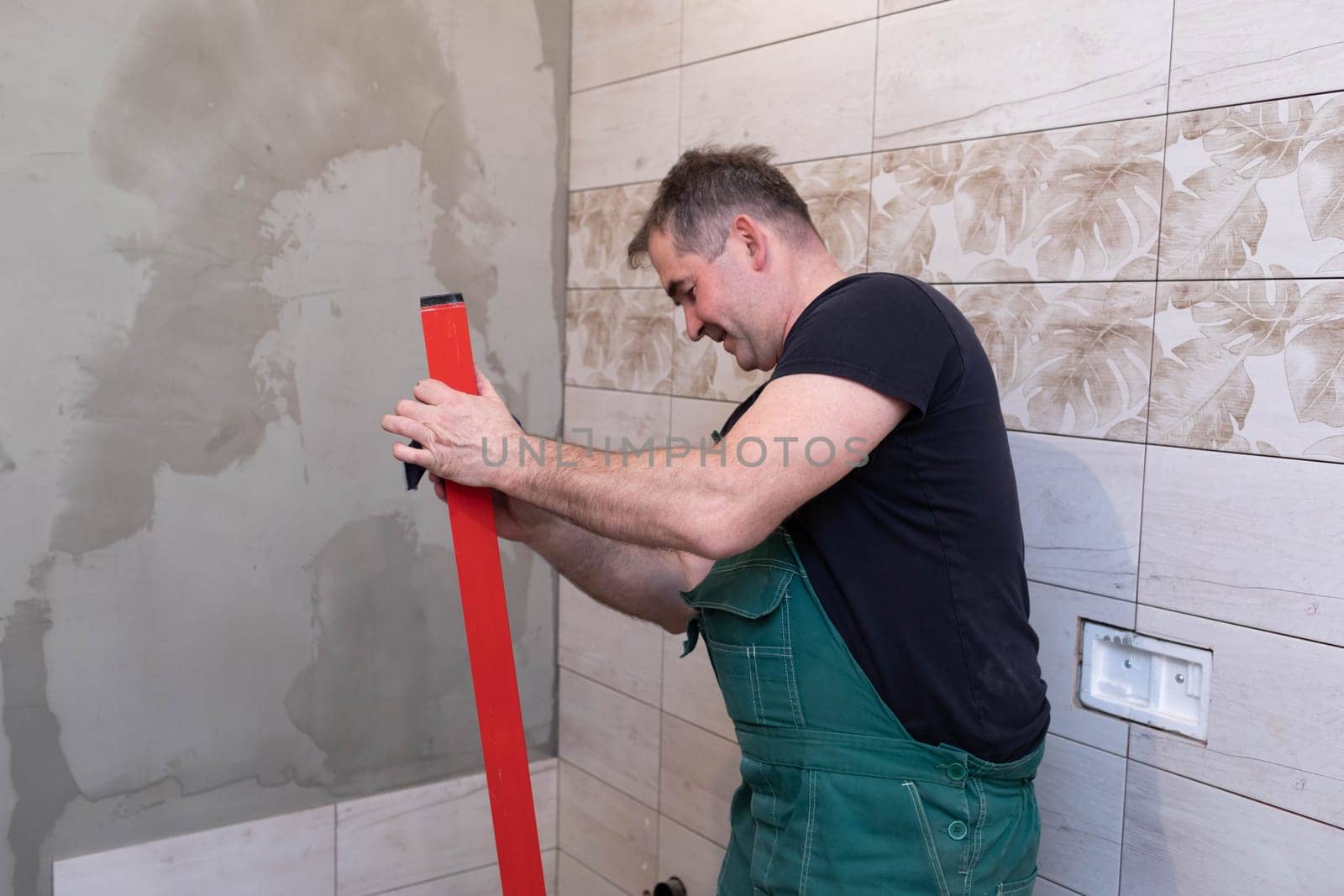 Red spirit level. Washes measuring tools with a wet cloth. Middle-aged manual worker. General construction worker.