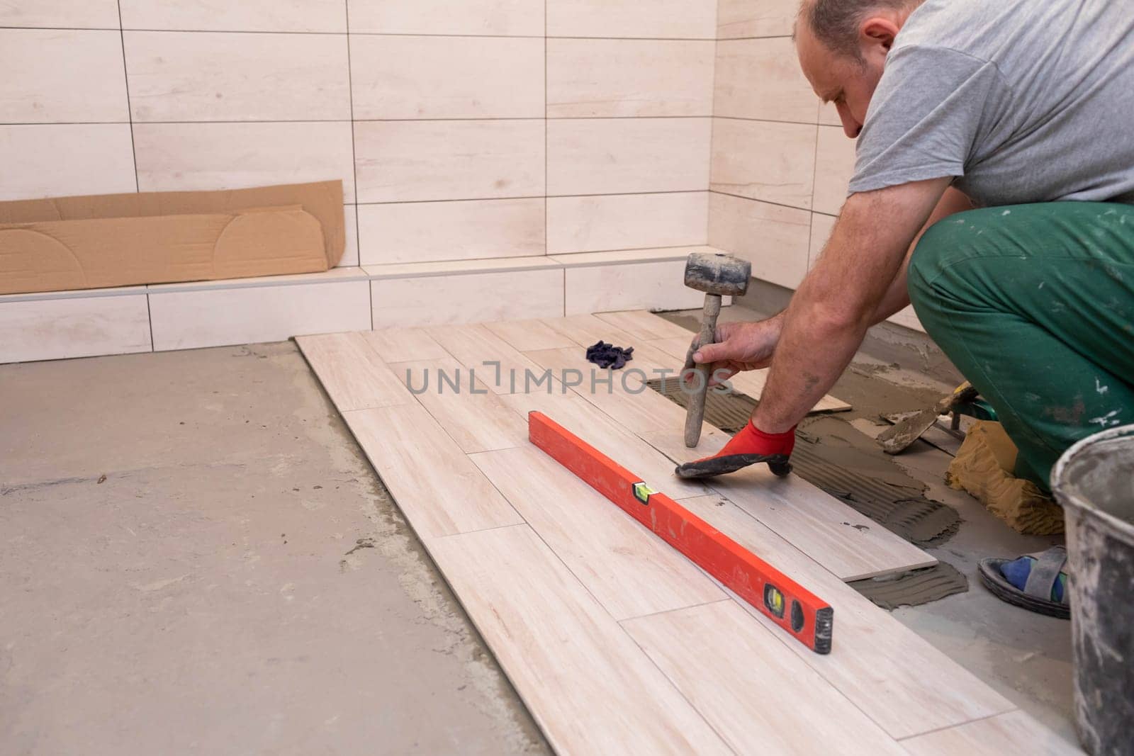 Professional construction worker laying ceramic tiles on the floor in the bathroom room.