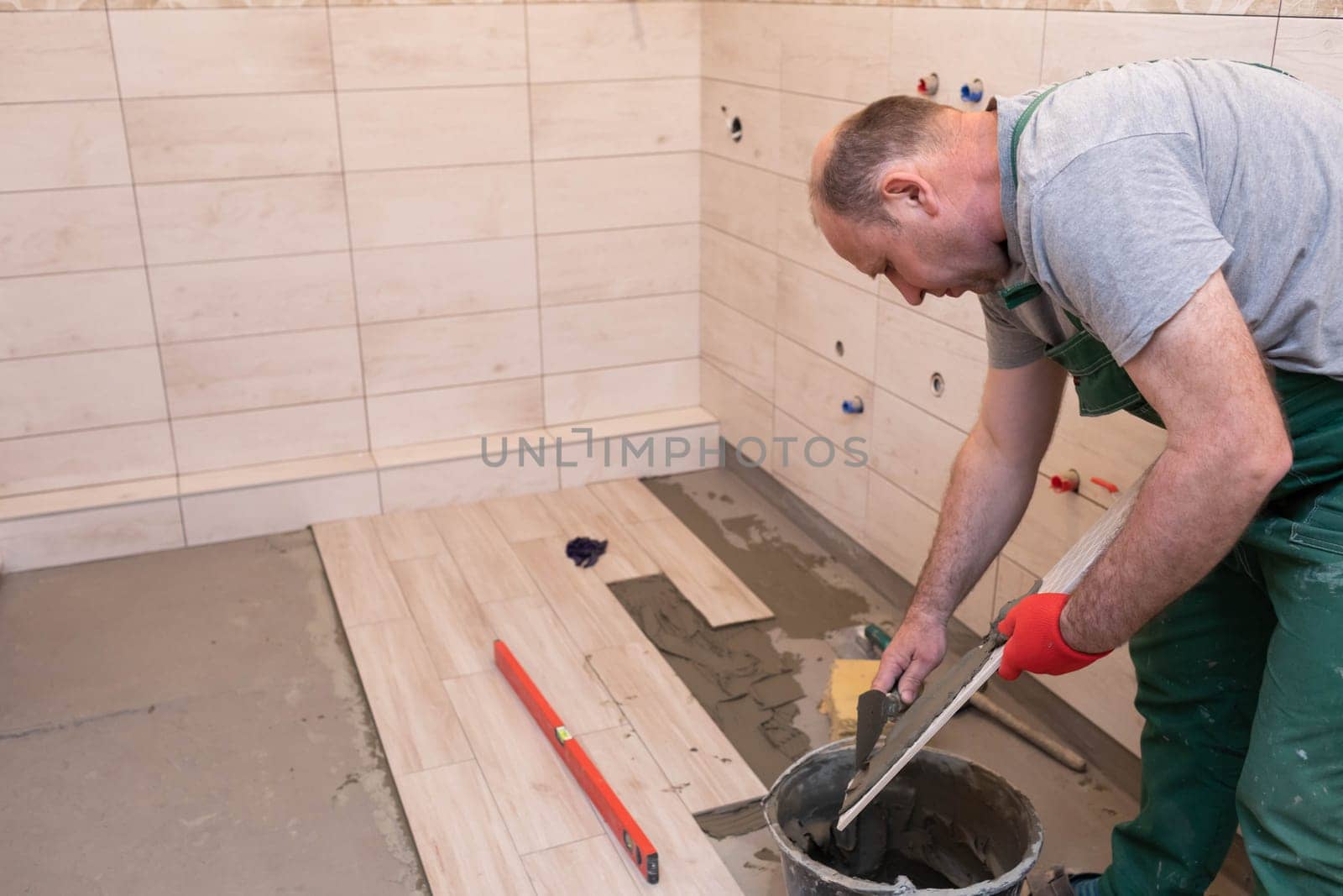 A construction worker lubricates the bottom of the ceramic tile with a metal trowel with special glue.