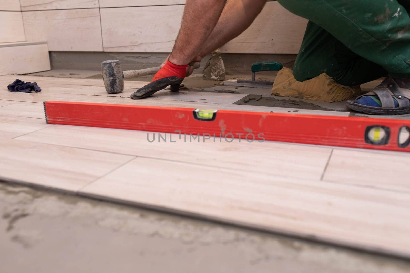 Rubber hammer. An experienced construction worker. Laying terracotta in the bathroom. Work clothes. He knocks with a hammer.