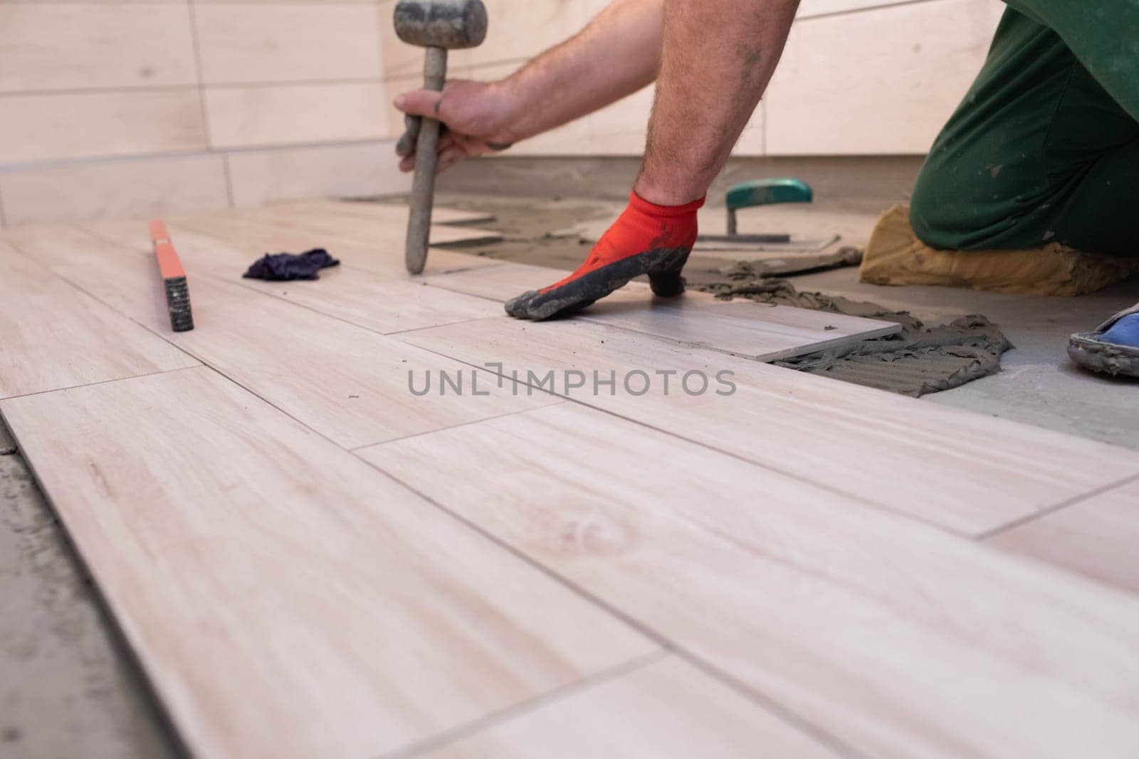 Rubber hammer. An experienced construction worker. Laying terracotta in the bathroom. Work clothes. He knocks with a hammer.