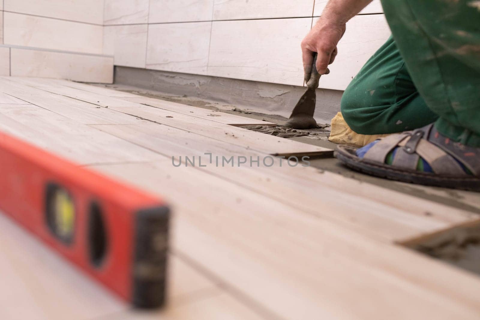 Professional construction worker laying ceramic tiles on the floor in the bathroom room.