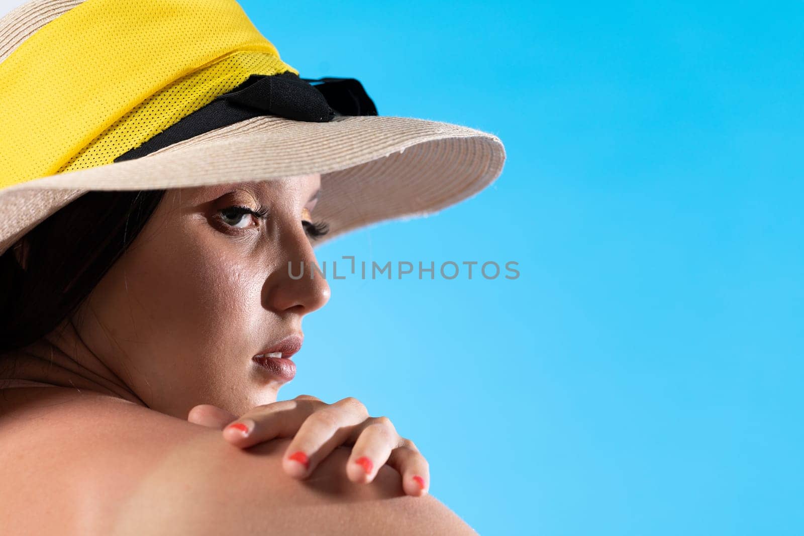 A young girl in a hat on a background of the blue sky with her hand holding her arm.