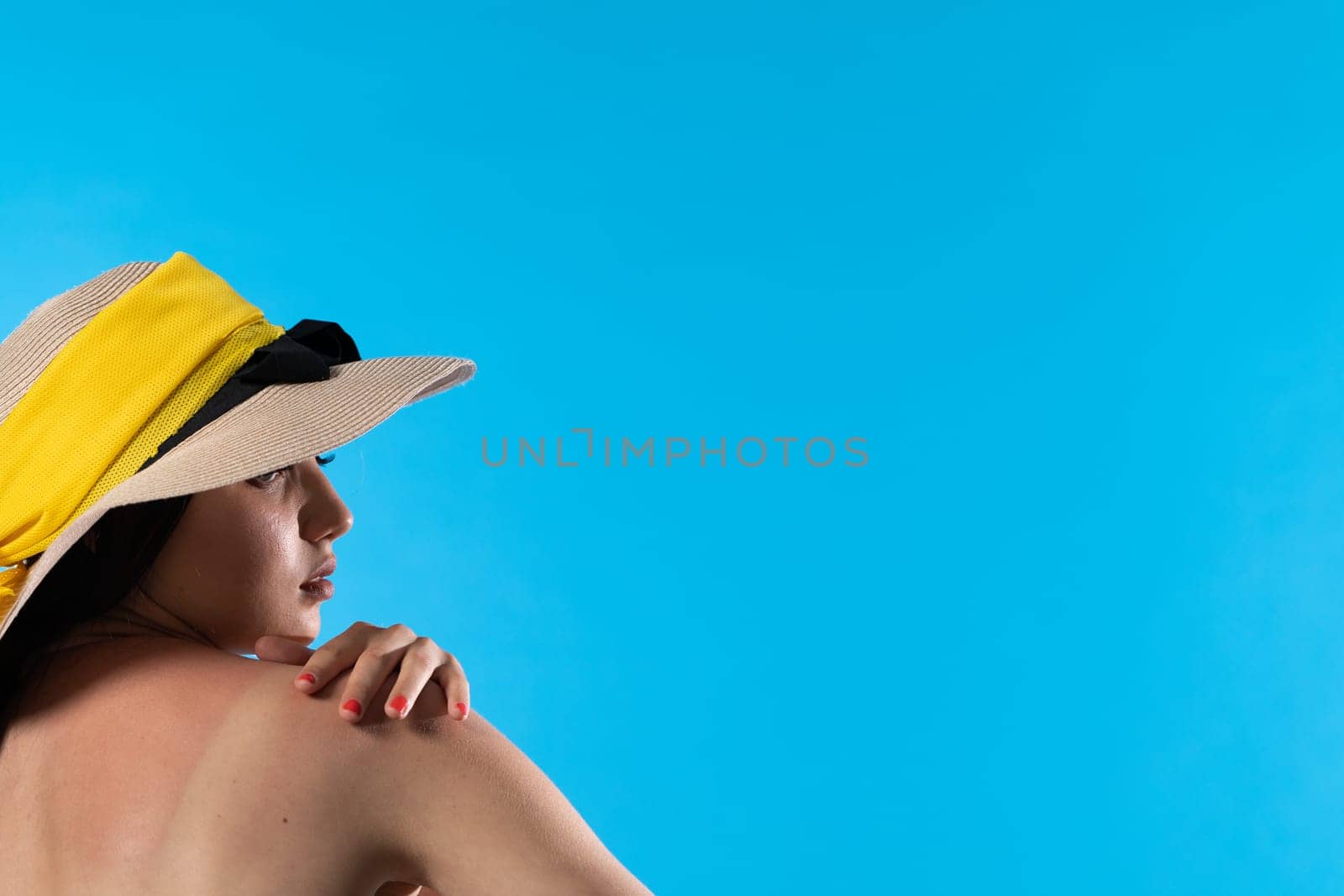 A young girl in a hat on a background of the blue sky with her hand holding her arm.