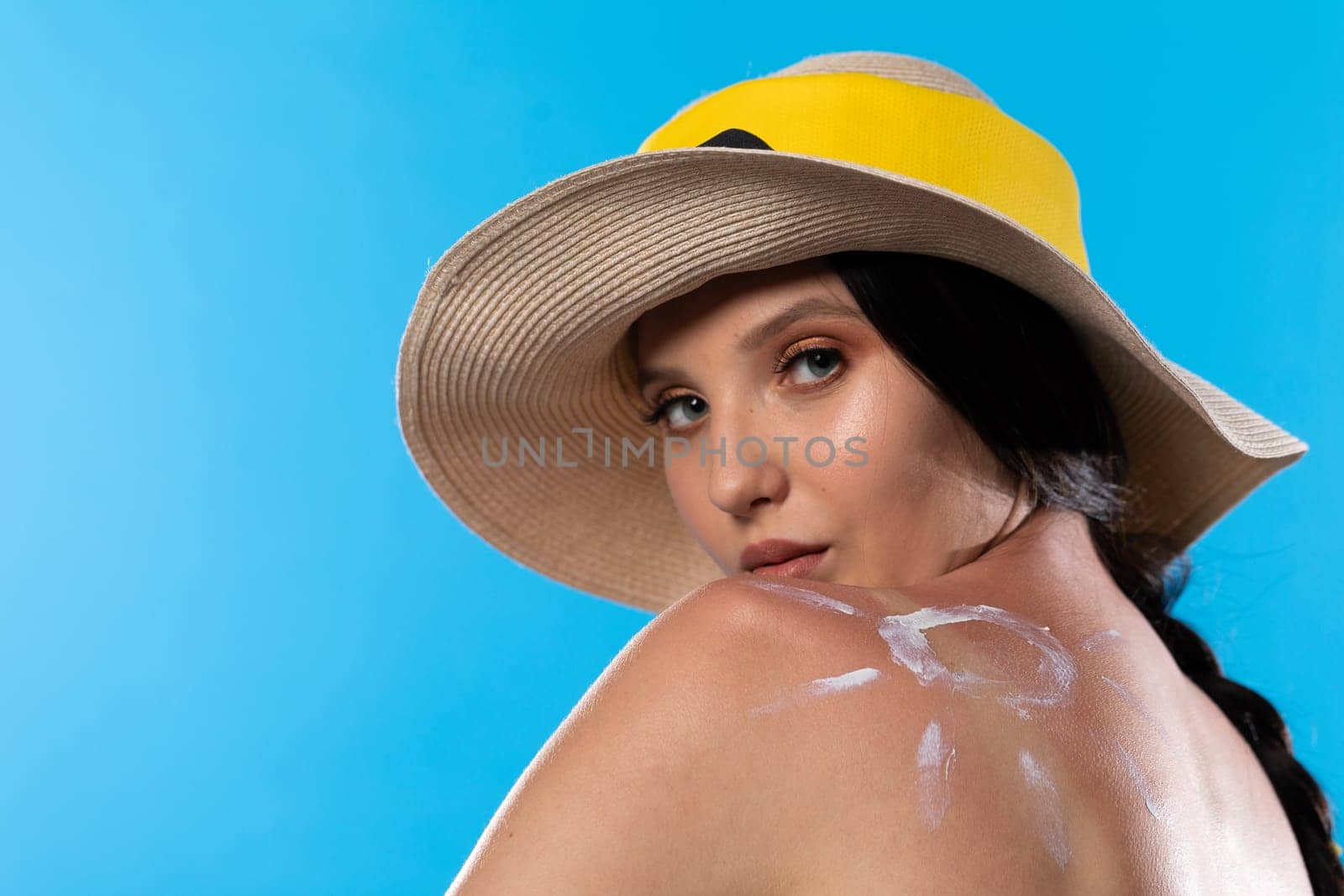A young girl on a sunny day with a hat on her head looks into the lens.