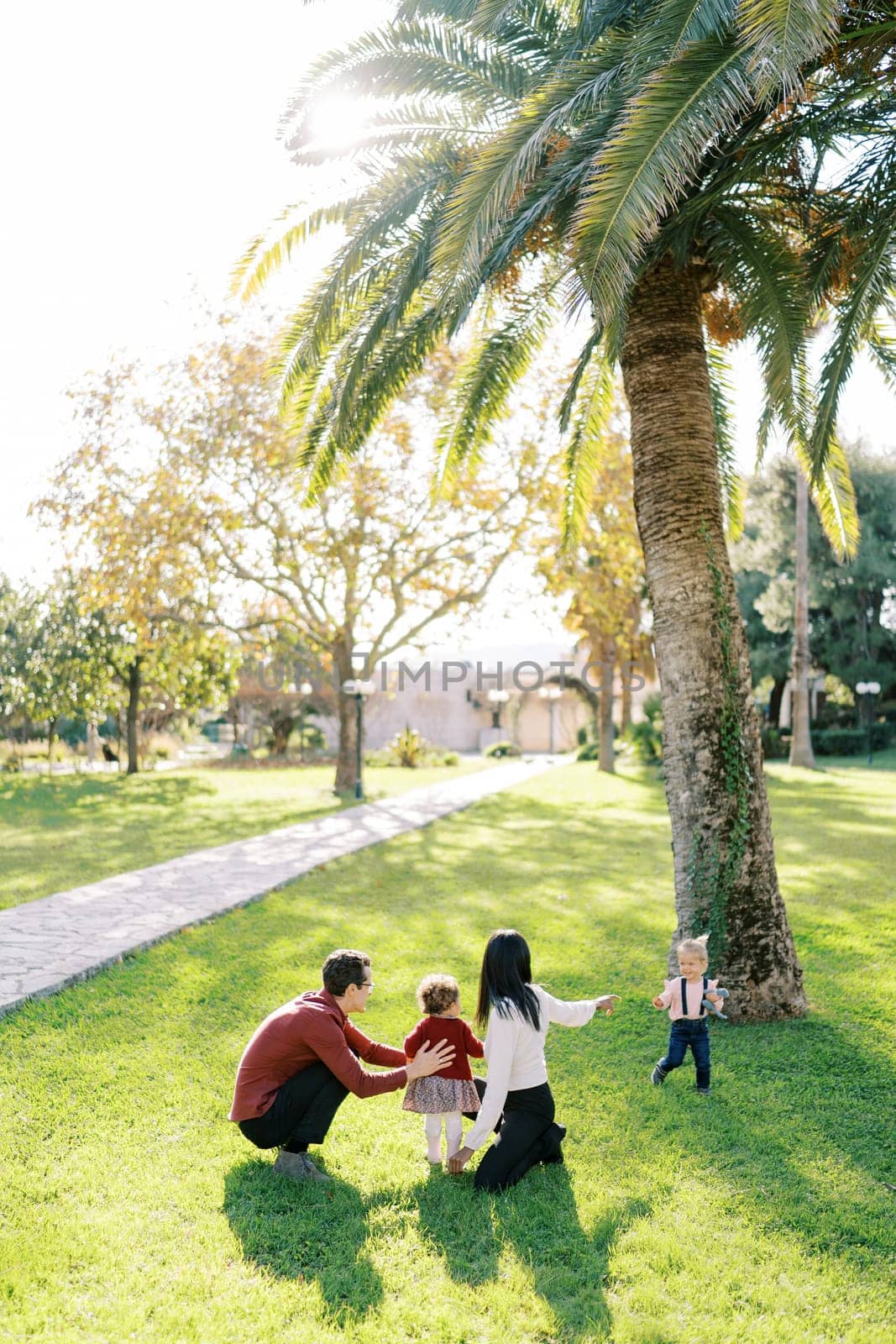 Parents with a little daughter squatted in the park in front of a small girl by Nadtochiy