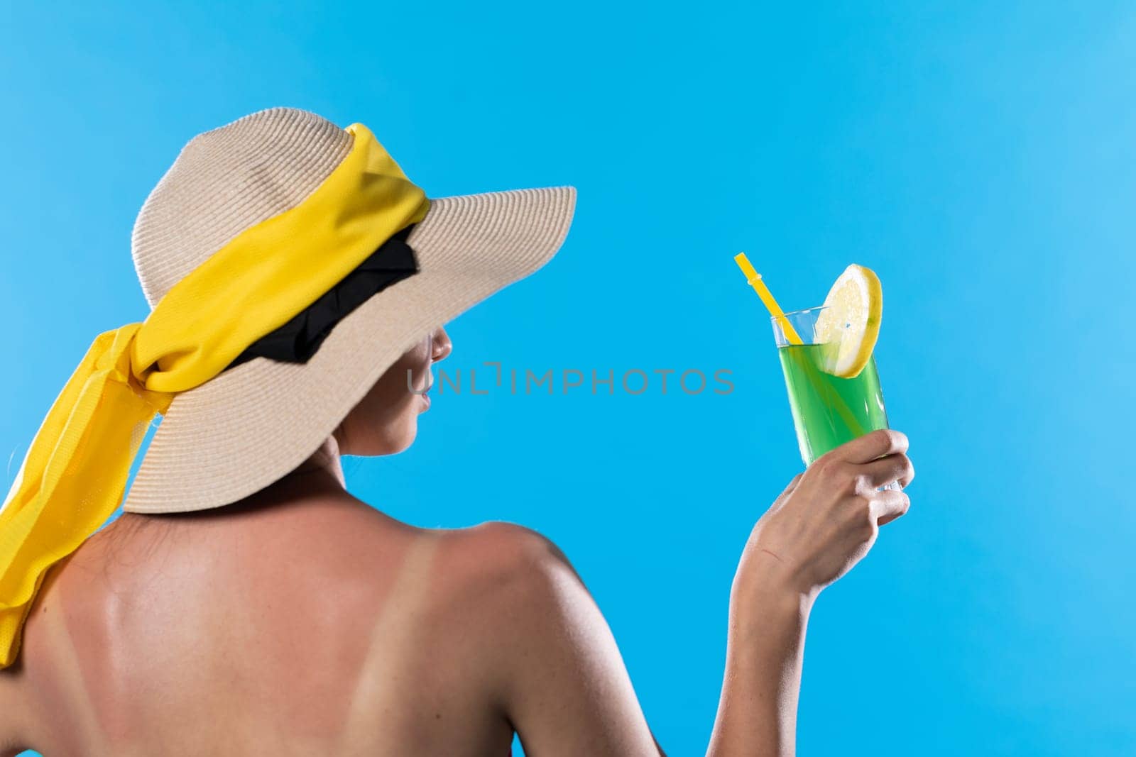 A young girl stands back to back with a cool drink in hand against the blue sky.