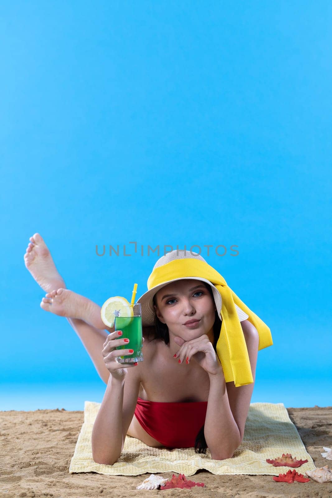 While sunbathing on the beach, a teenager drinks a cold alcoholic drink.