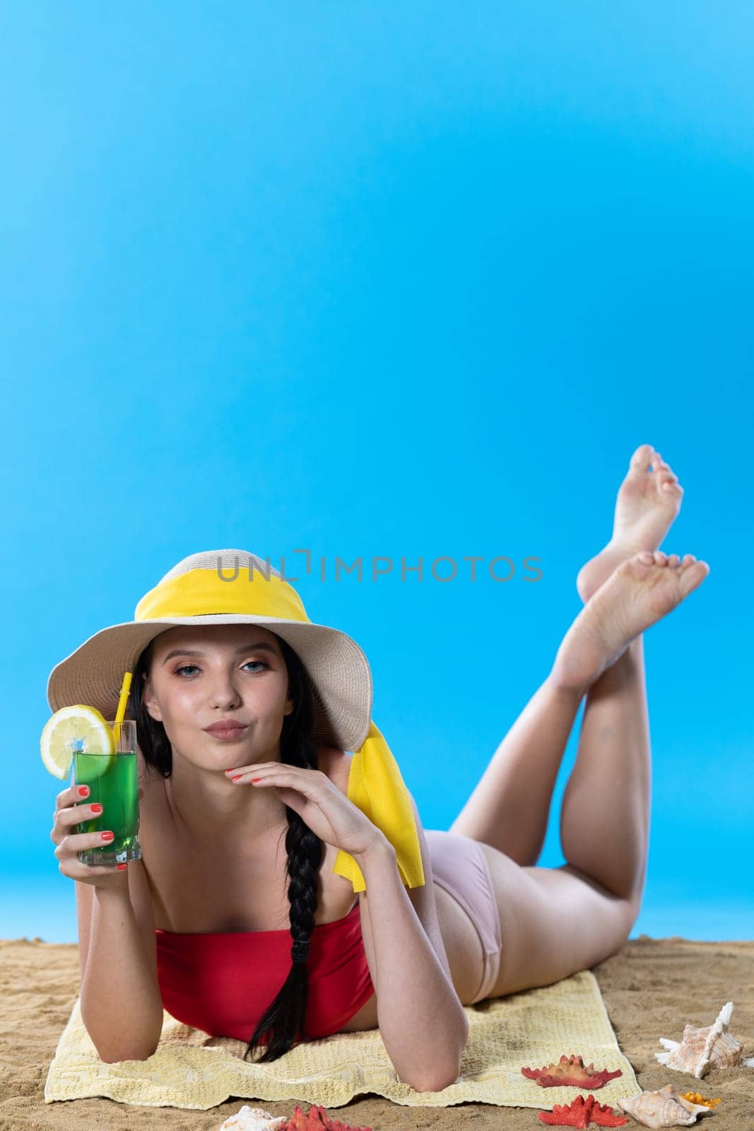 A young teenager is lying on the beach with an alcoholic drink and sunbathing in the summer sun. by fotodrobik