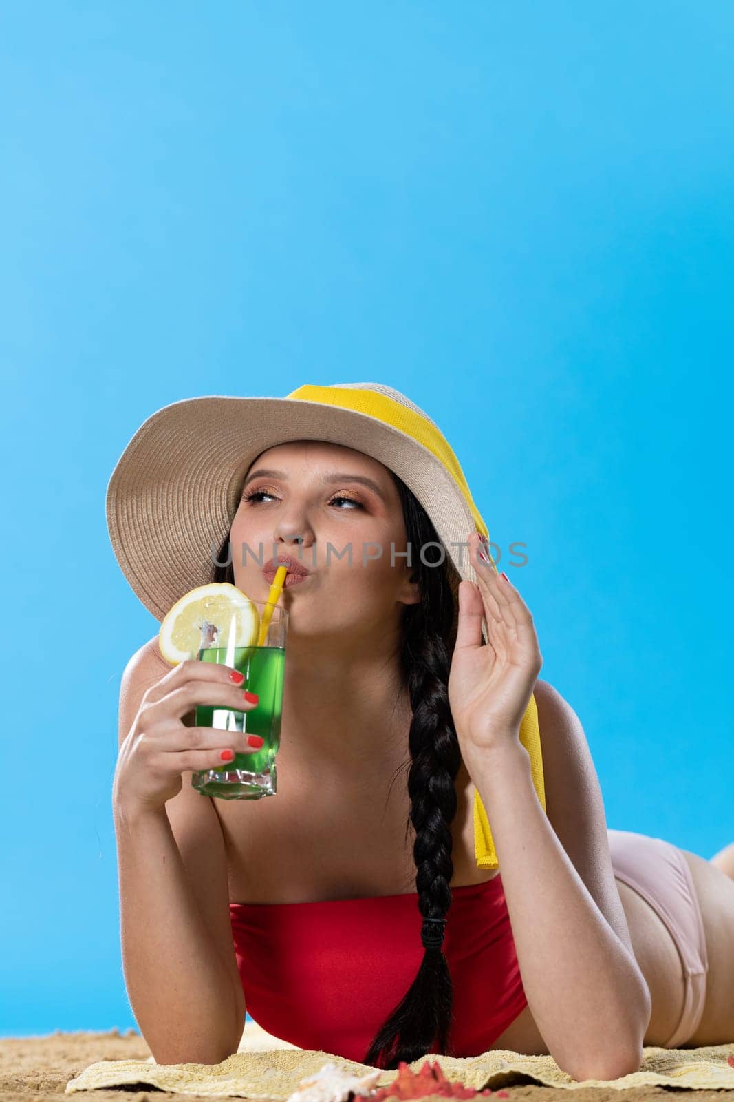 While sunbathing on the beach, a teenager drinks a cold alcoholic drink.