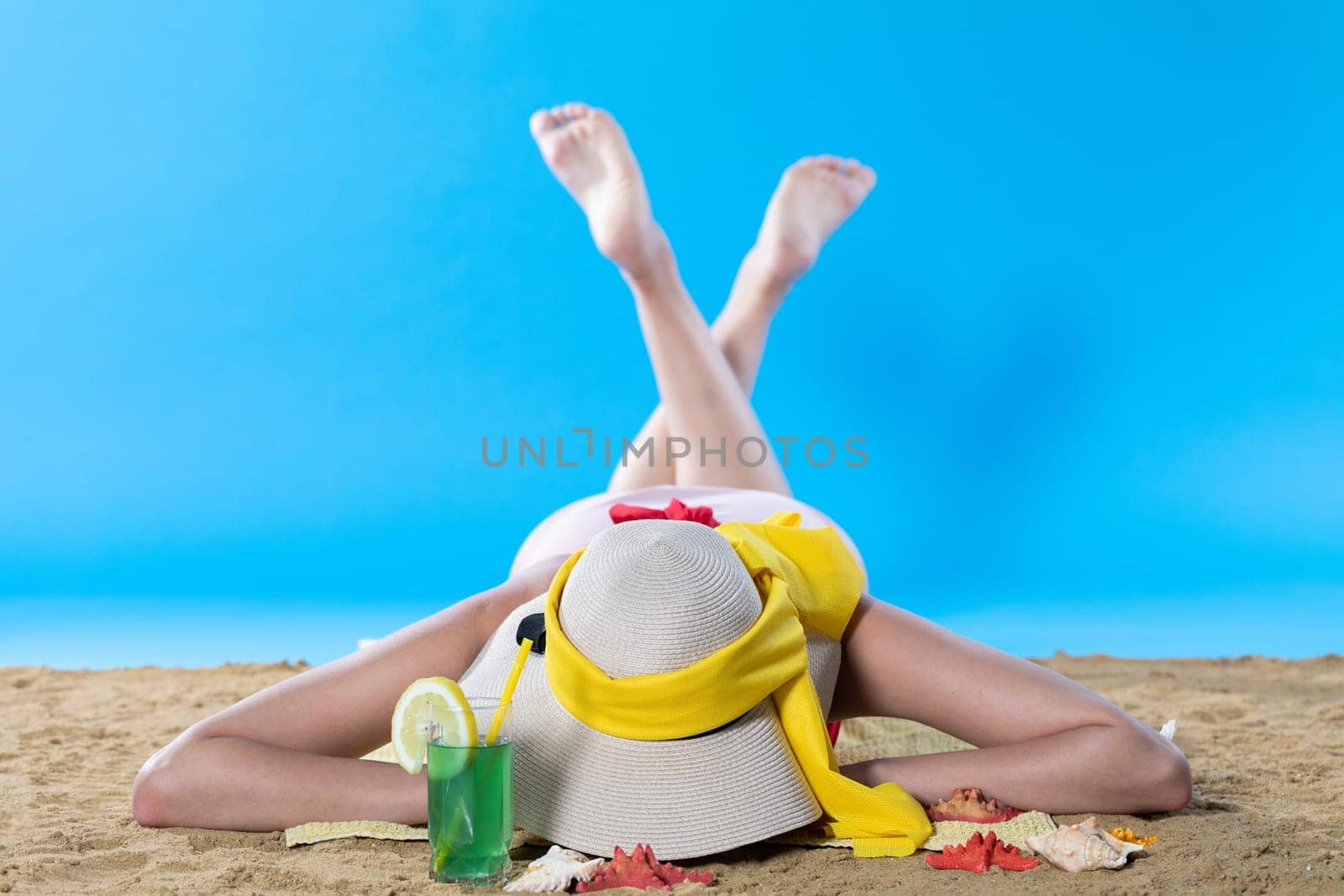 While sunbathing on the beach, a teenager drinks a cold alcoholic drink.
