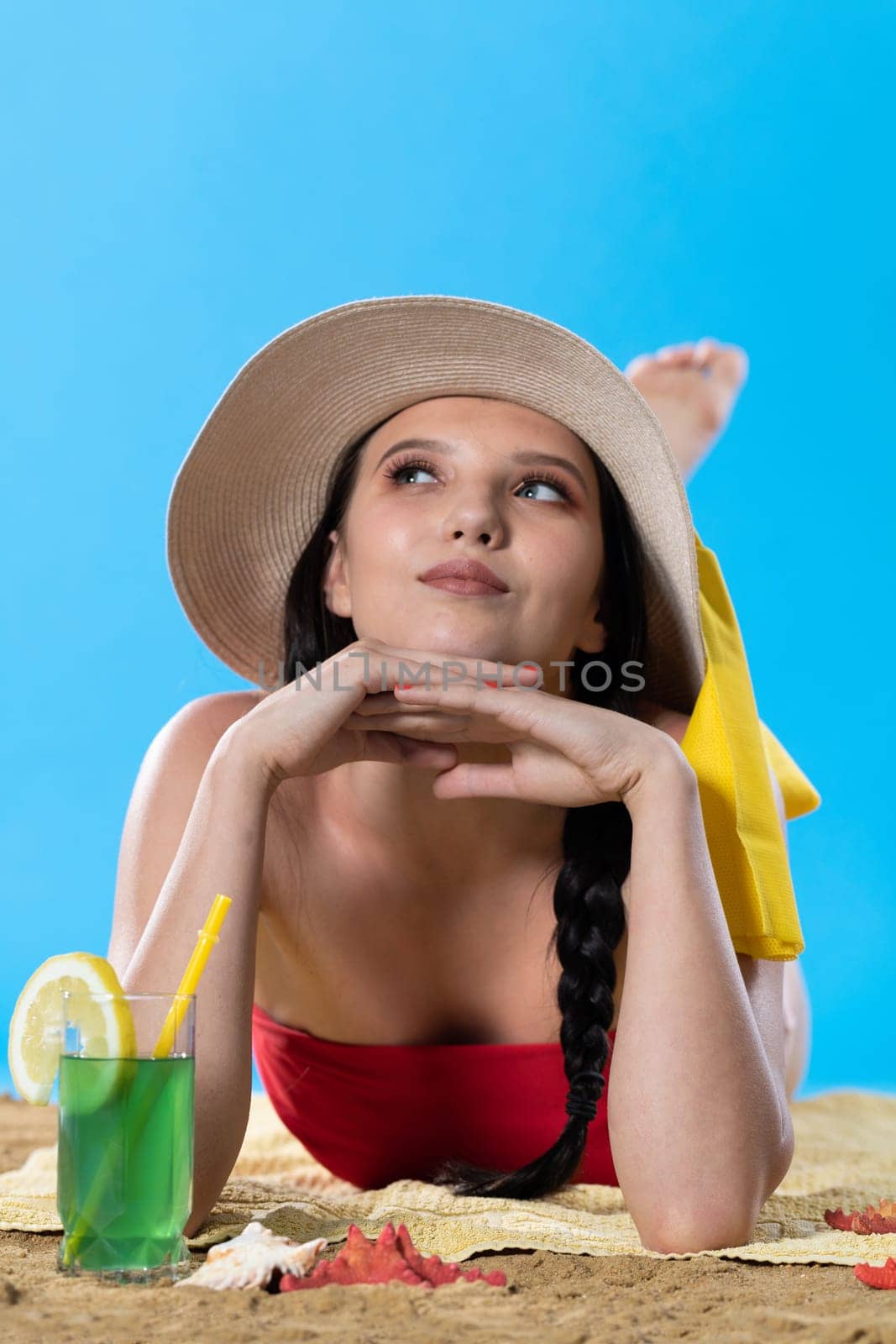 While sunbathing on the beach, a teenager drinks a cold alcoholic drink.