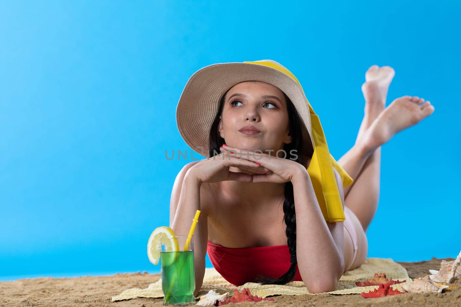While sunbathing on the beach, a teenager drinks a cold alcoholic drink.