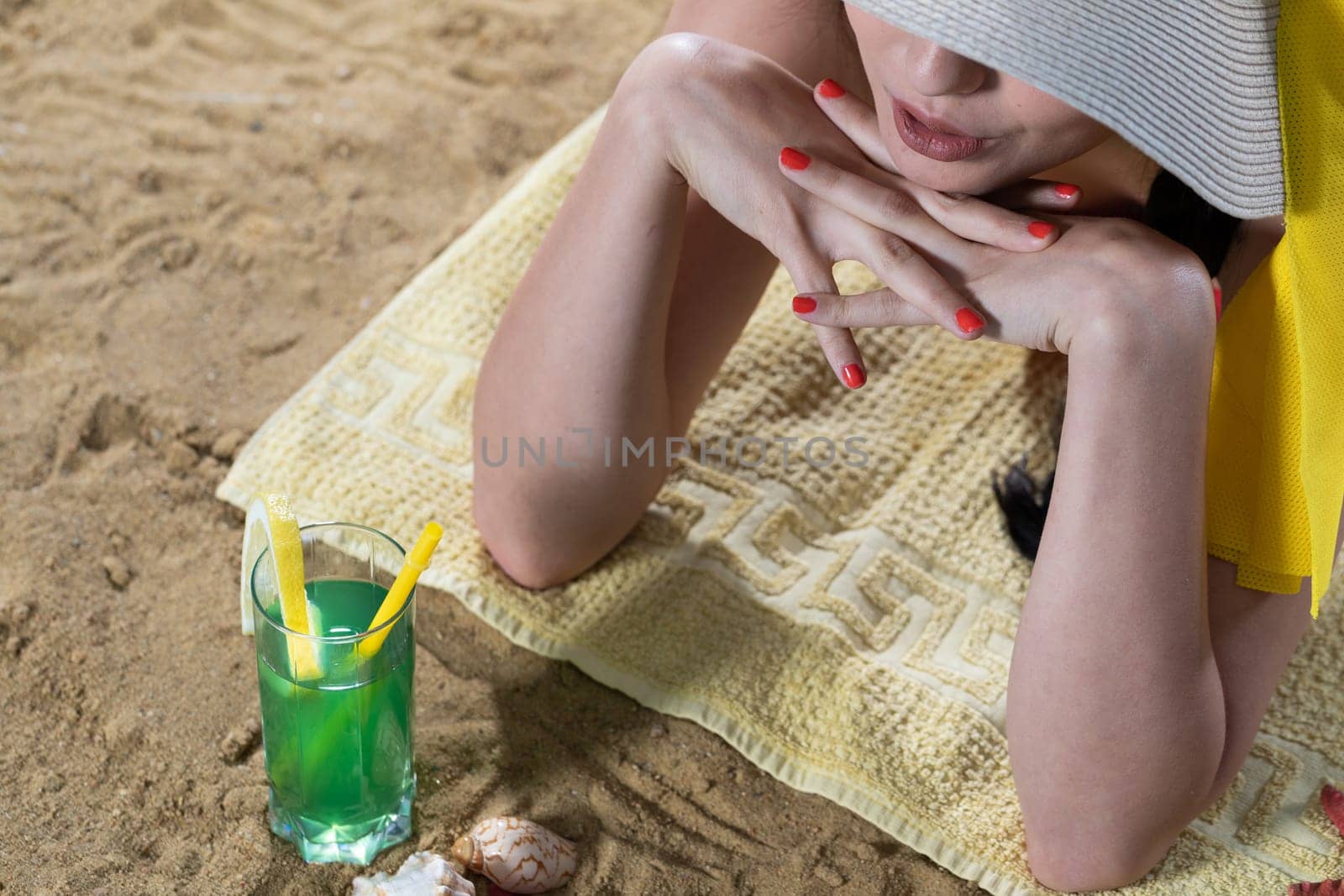While sunbathing on the beach, a teenager drinks a cold alcoholic drink.