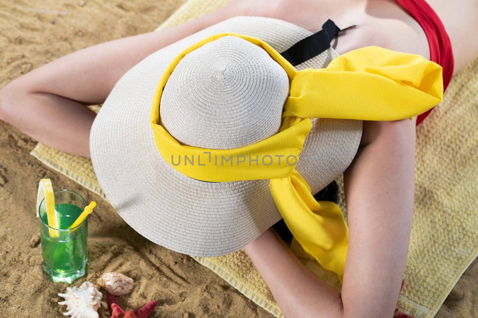 While sunbathing on the beach, a teenager drinks a cold alcoholic drink.