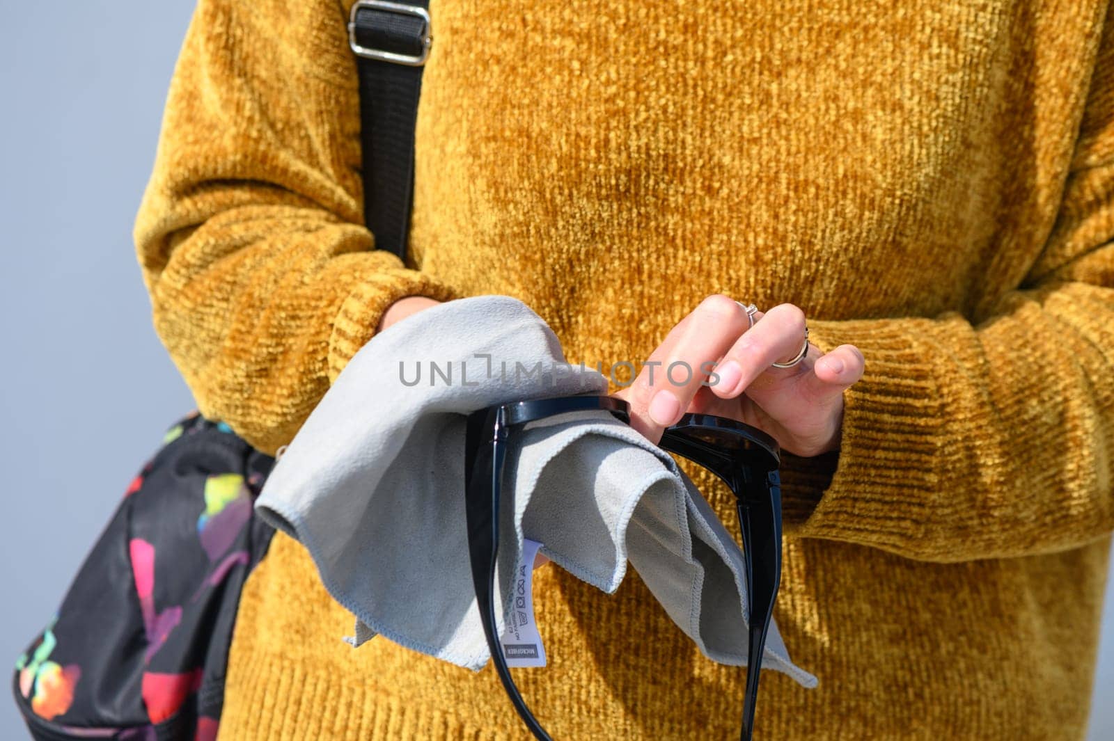 Woman wiping sunglasses with microfiber cloth on light background, close-up 1