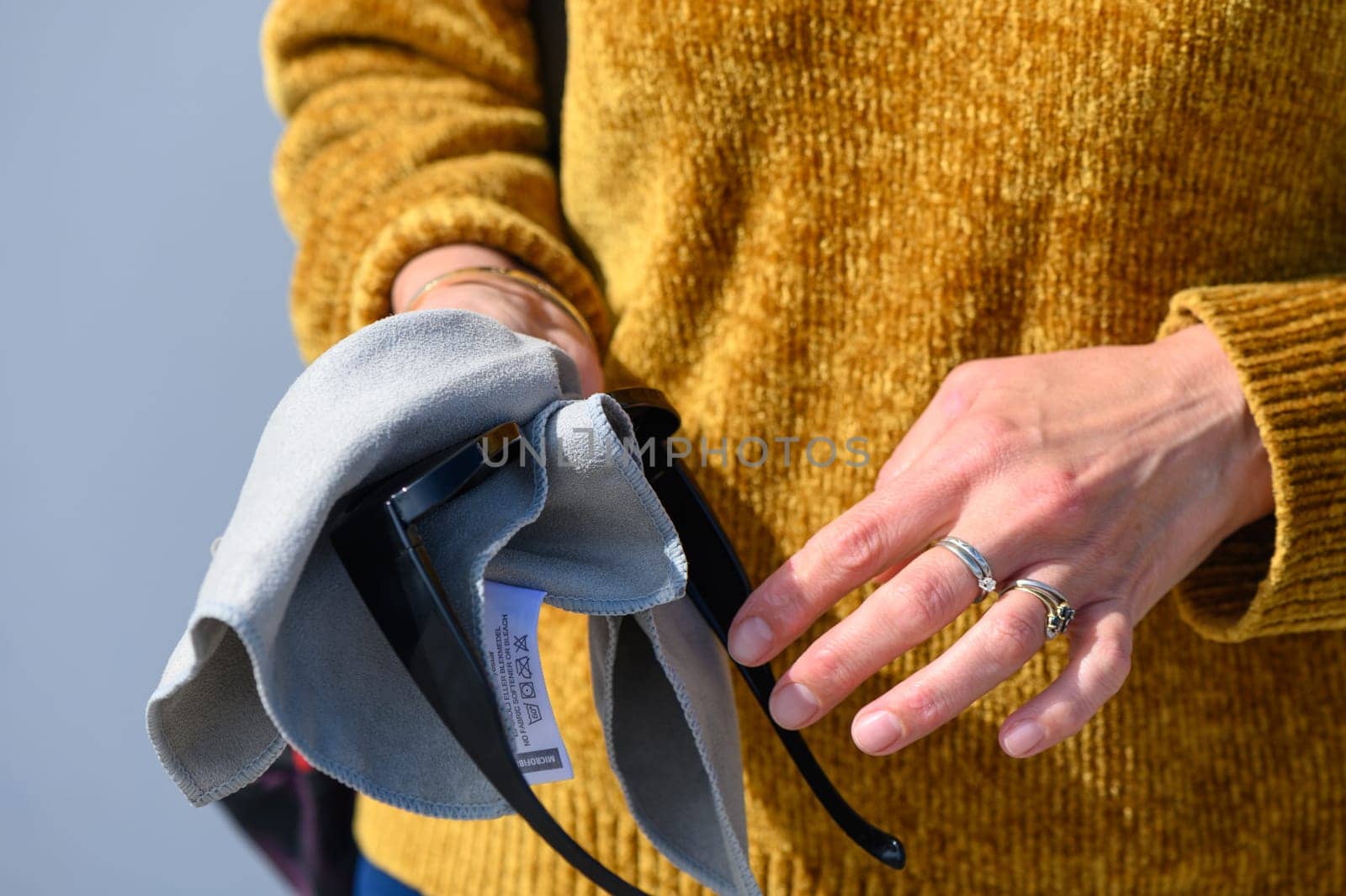 Woman wiping sunglasses with microfiber cloth on light background, close-up