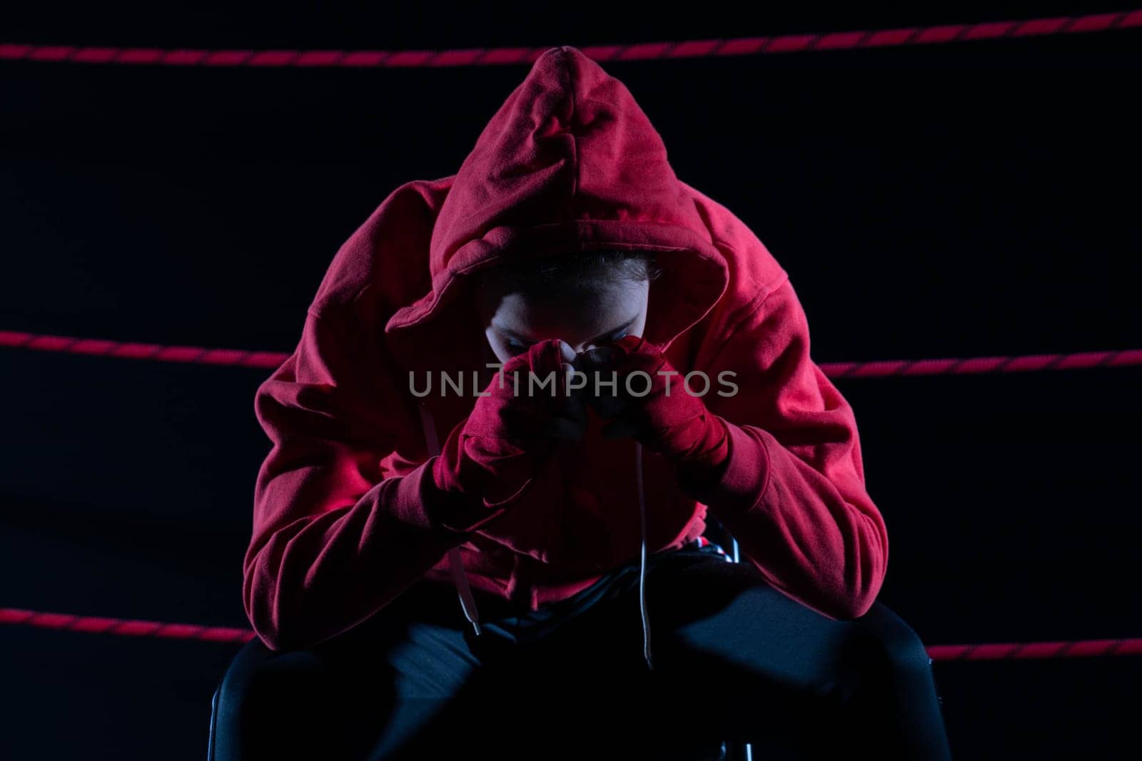 A lost fight of a strong player. He is sitting in a chair. Right after losing the fight. Sad woman after a fight in the ring. In a hoodie.