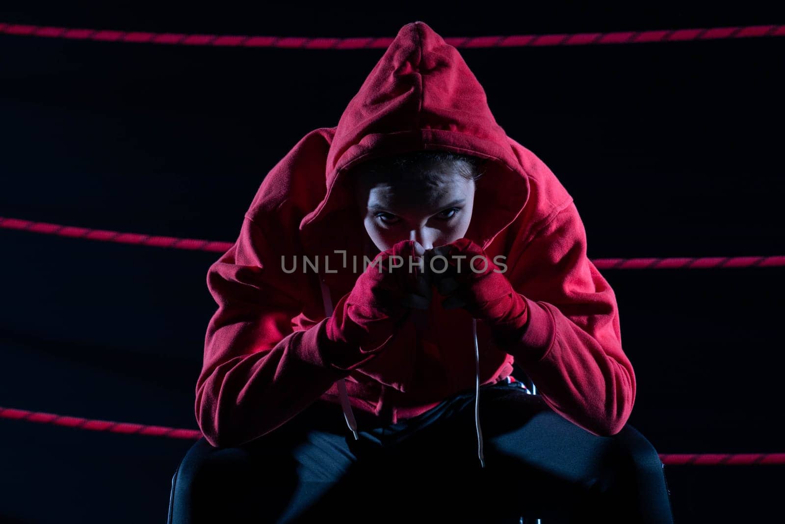 A lost fight of a strong player. He is sitting in a chair. Right after losing the fight. Sad woman after a fight in the ring. In a hoodie.