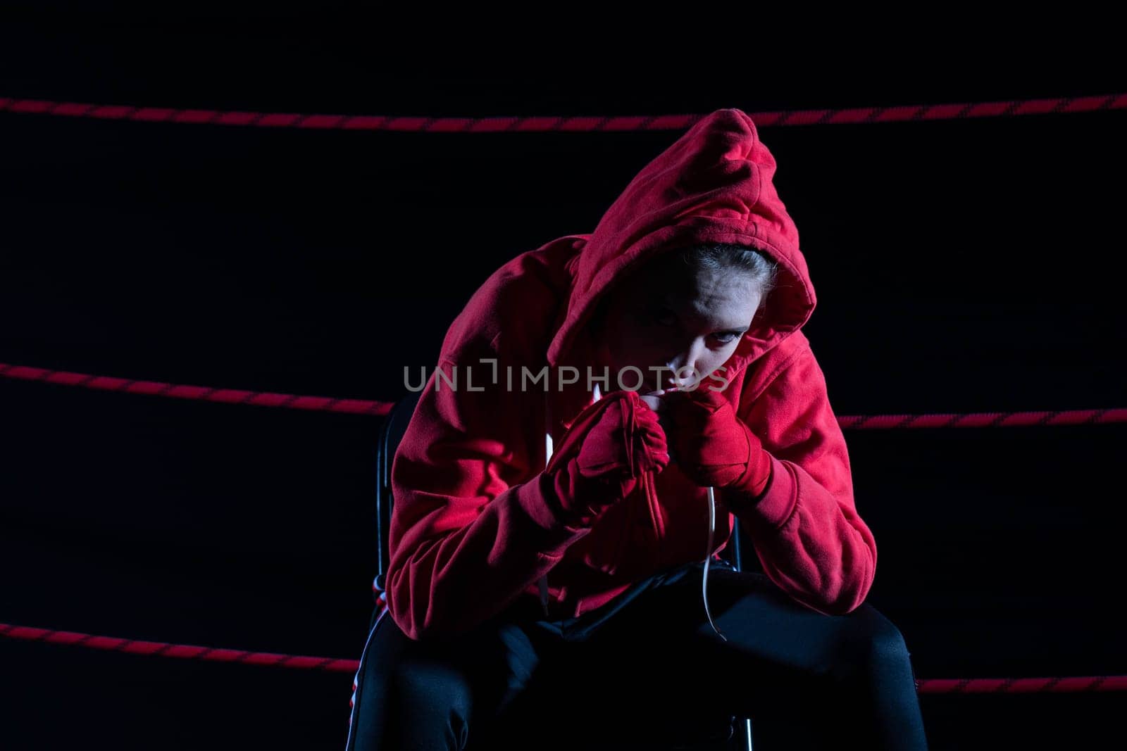 A lost fight of a strong player. He is sitting in a chair. Right after losing the fight. Sad woman after a fight in the ring. In a hoodie.
