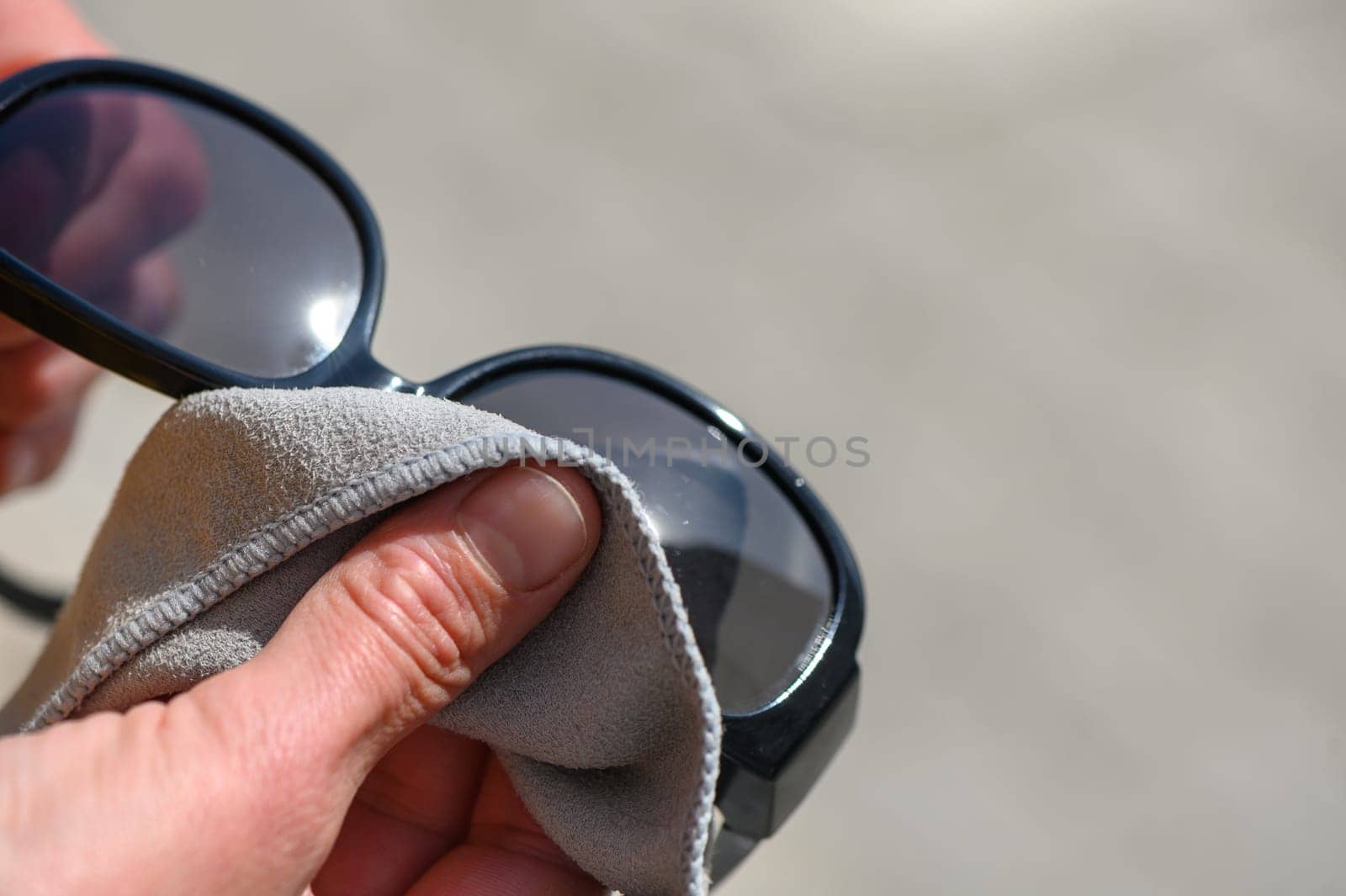 Woman wiping sunglasses with microfiber cloth on light background, close-up 2