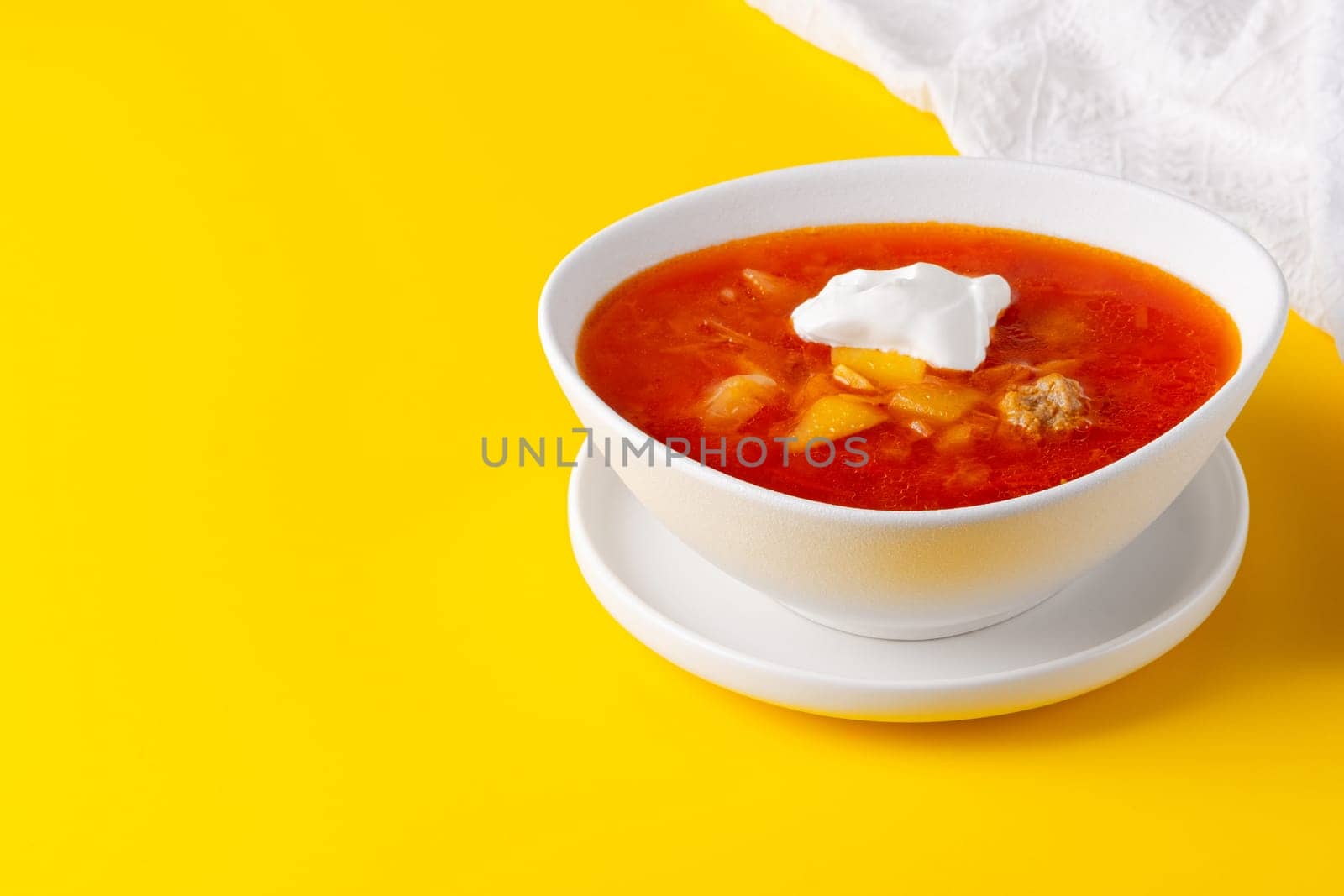 Red borscht in bowl on a yellow background, traditional dish that is cooked with broth, with copy space for text by NataliPopova
