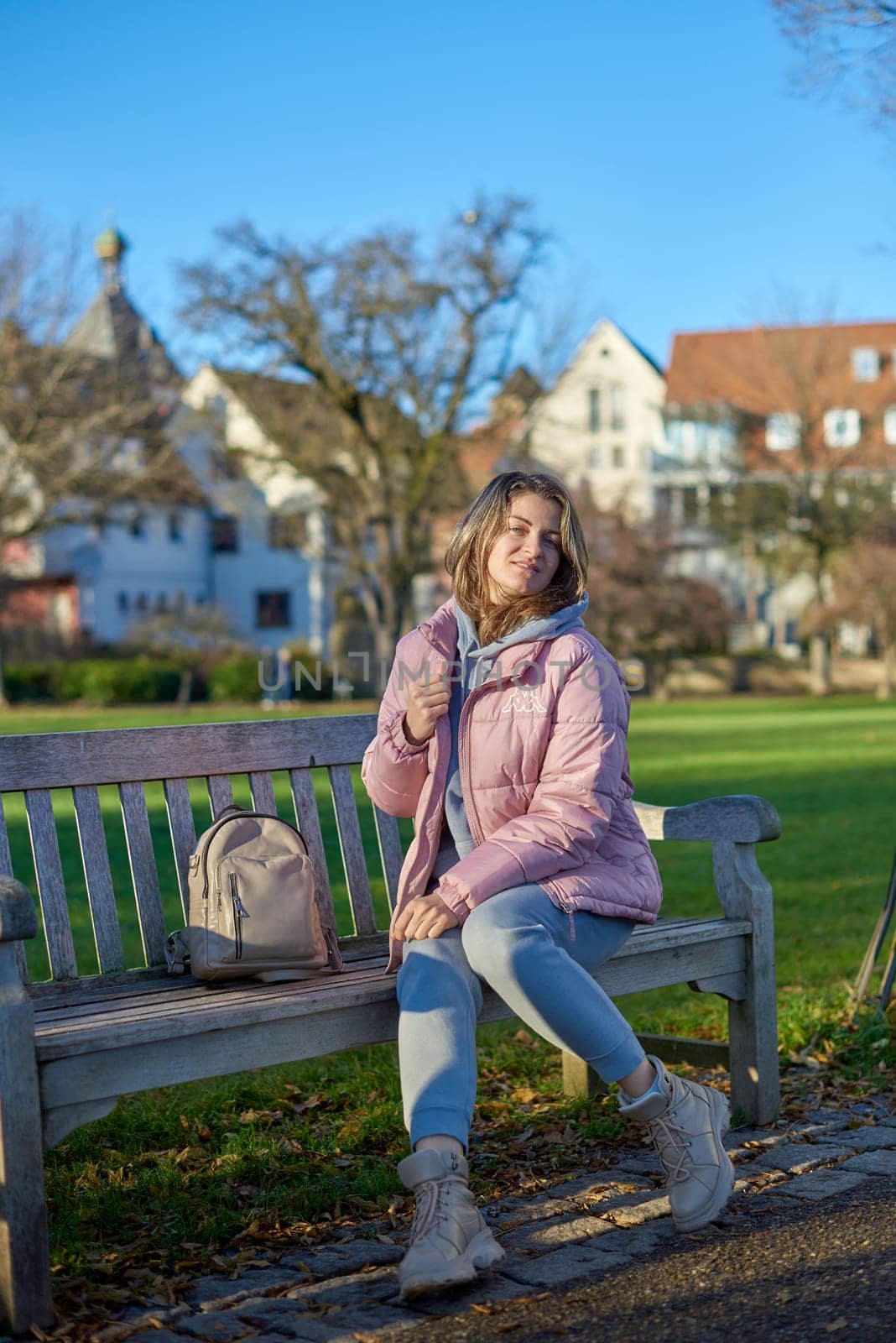 Winter Joy in Bitigheim-Bissingen: Beautiful Girl in Pink Jacket Sitting Amidst Half-Timbered Charm. beautiful girl in a pink winter jacket sitting on a bench in a park, set against the backdrop of the historic town of Bitigheim-Bissingen, Baden-Württemberg, Germany. by Andrii_Ko