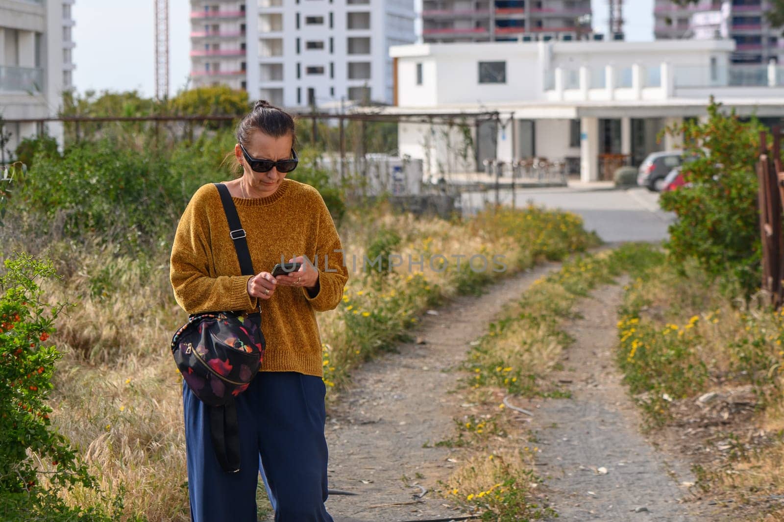 woman holding a mobile phone with, standing or walking against the background of houses. 1 by Mixa74