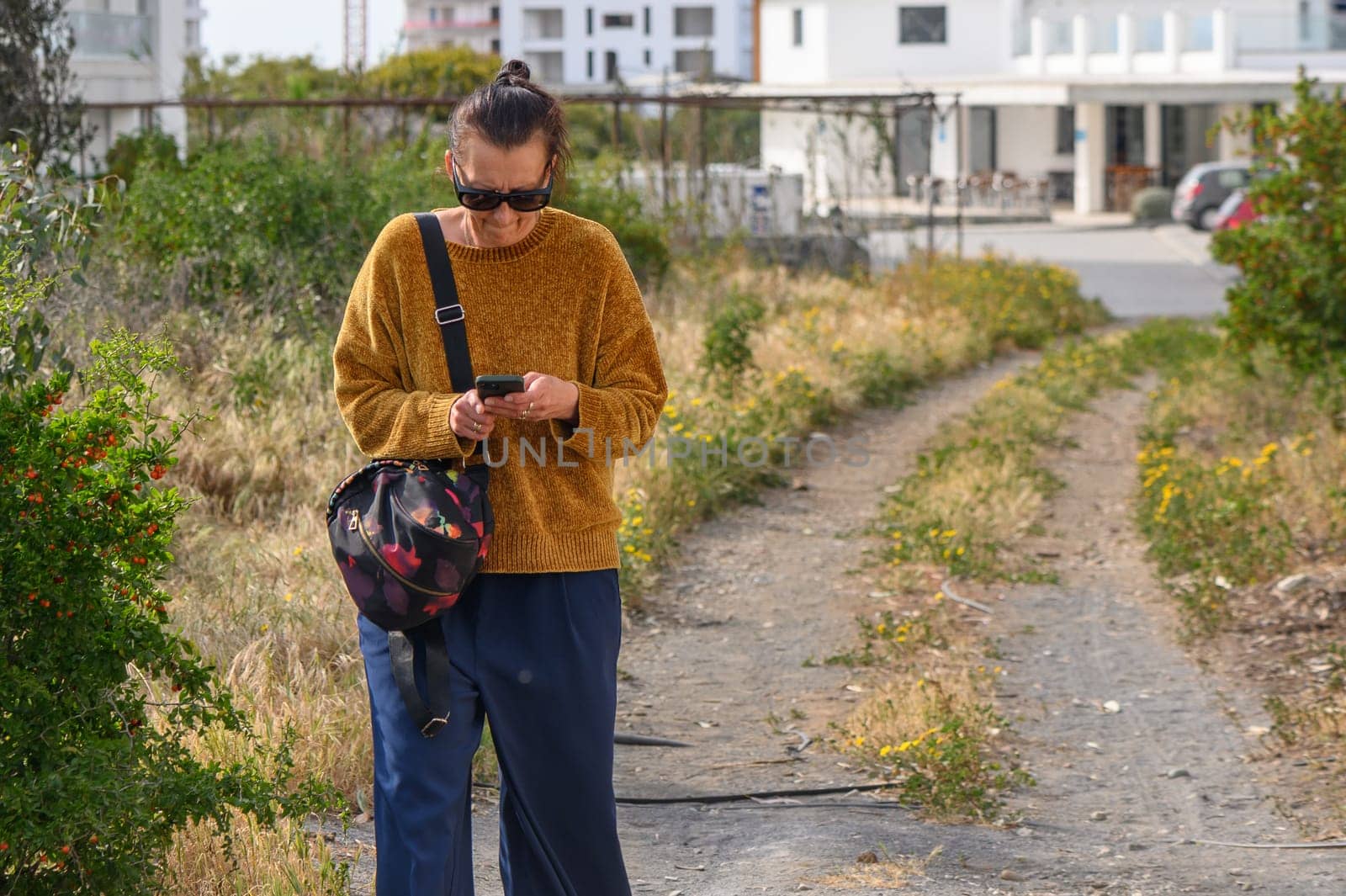 woman holding a mobile phone with, standing or walking against the background of houses.