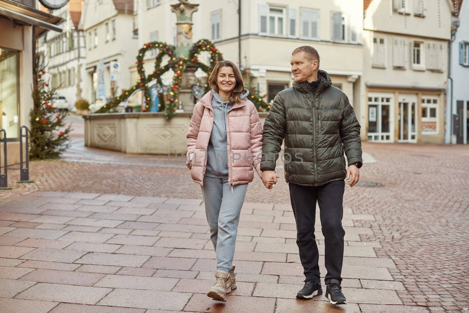 Loving couple of tourists walking around old town. Couple of lovers leisurely stroll in the cool autumn morning on the streets of a BIETIGHEIM-BISSINGEN (Germany). The guy holds his wife. Vacation, Winter, holiday. Romantic Stroll through Historic German Charm. Couple Walking in Europe's Old Town by Andrii_Ko