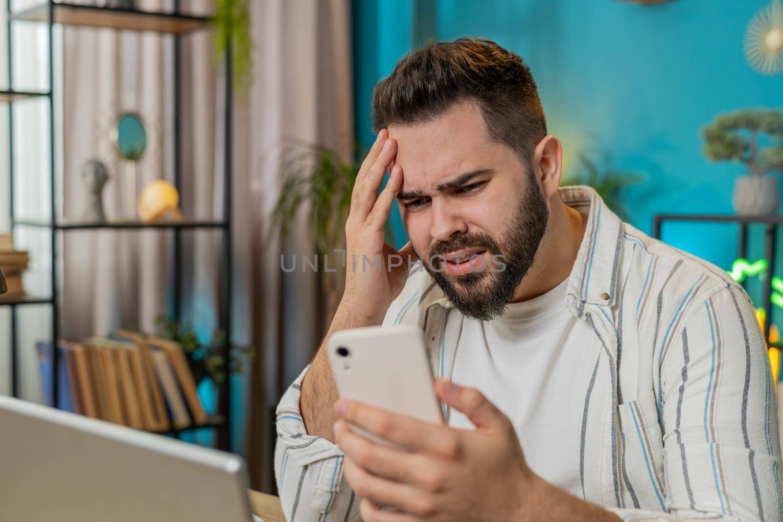 Caucasian young business man using smartphone typing browsing loses becoming surprised sudden lottery results bad news fortune loss fail at home office desk workplace. Freelancer worker guy. Lifestyle