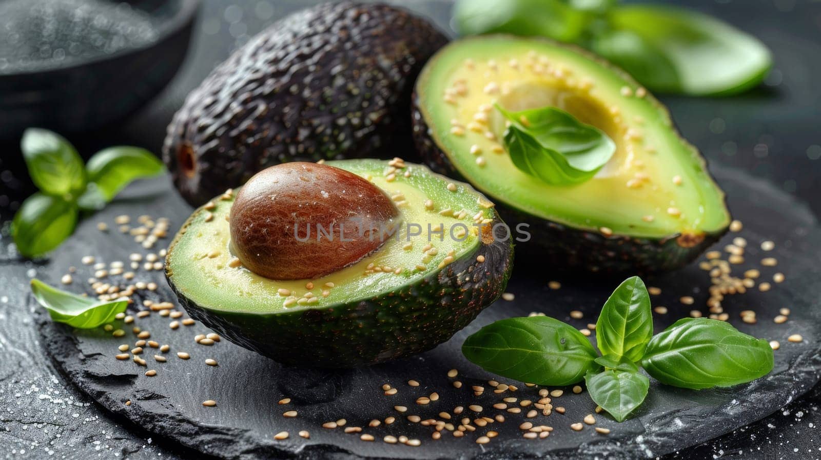 Avocado halves with seeds and leaves on a black plate