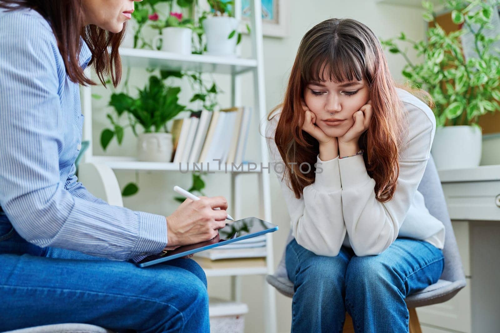 Sad, serious teenage girl at session in office of mental professional, psychologist, counselor, social worker. Feelings, difficulties, problems, depression, stress youth concept