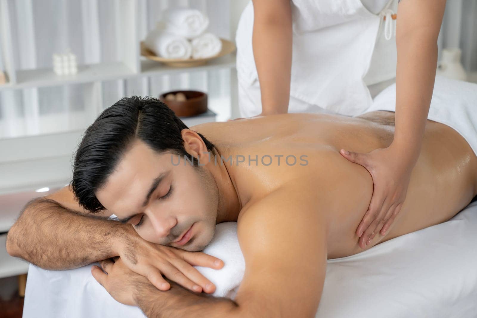 Caucasian man customer enjoying relaxing anti-stress spa massage and pampering with beauty skin recreation leisure in day light ambient salon spa at luxury resort or hotel. Quiescent