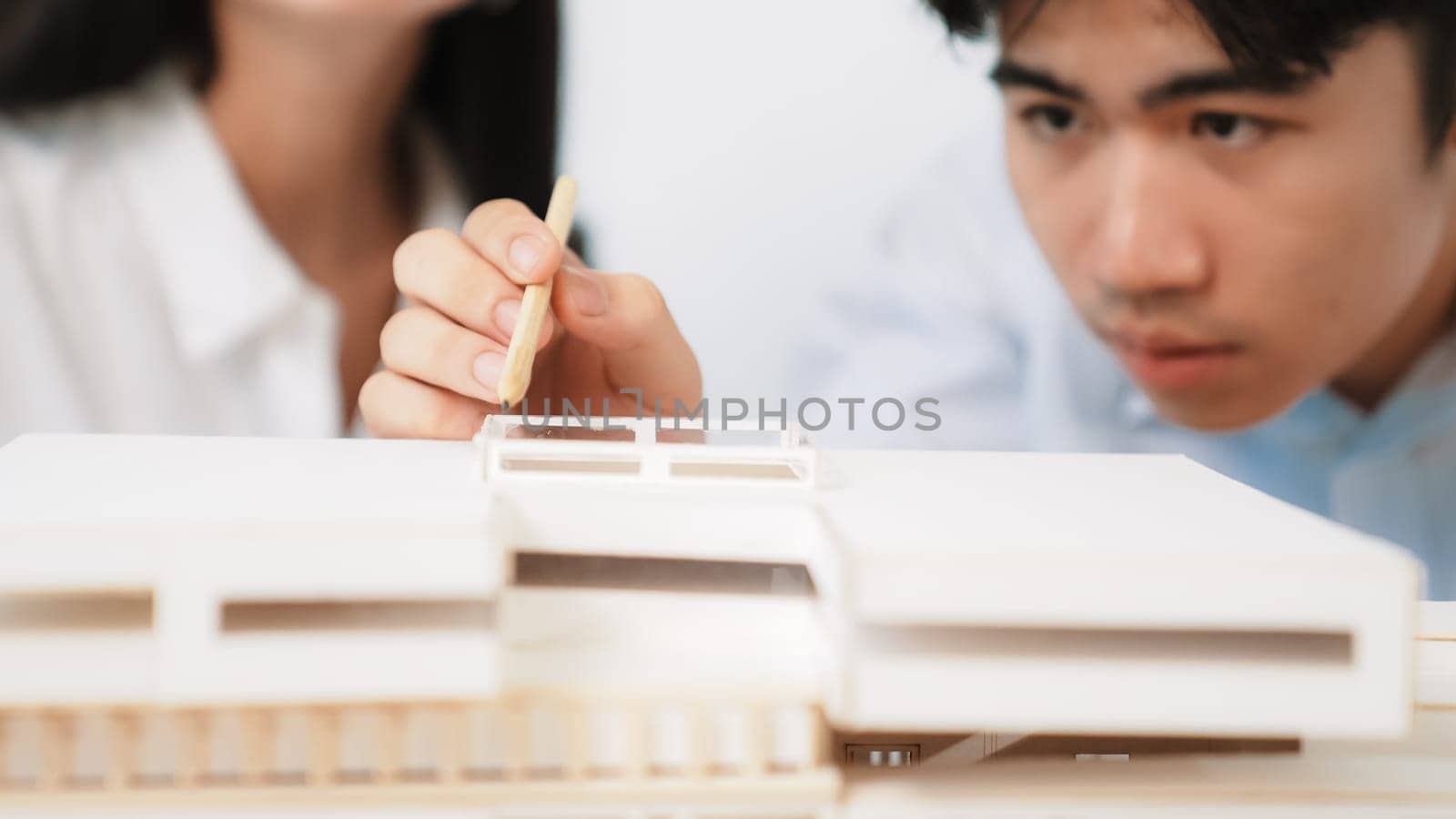 Closeup of young professional architect team work together to use pencil testing house model durability about house construction. Creative design and teamwork concept. Focus on hand. Immaculate.