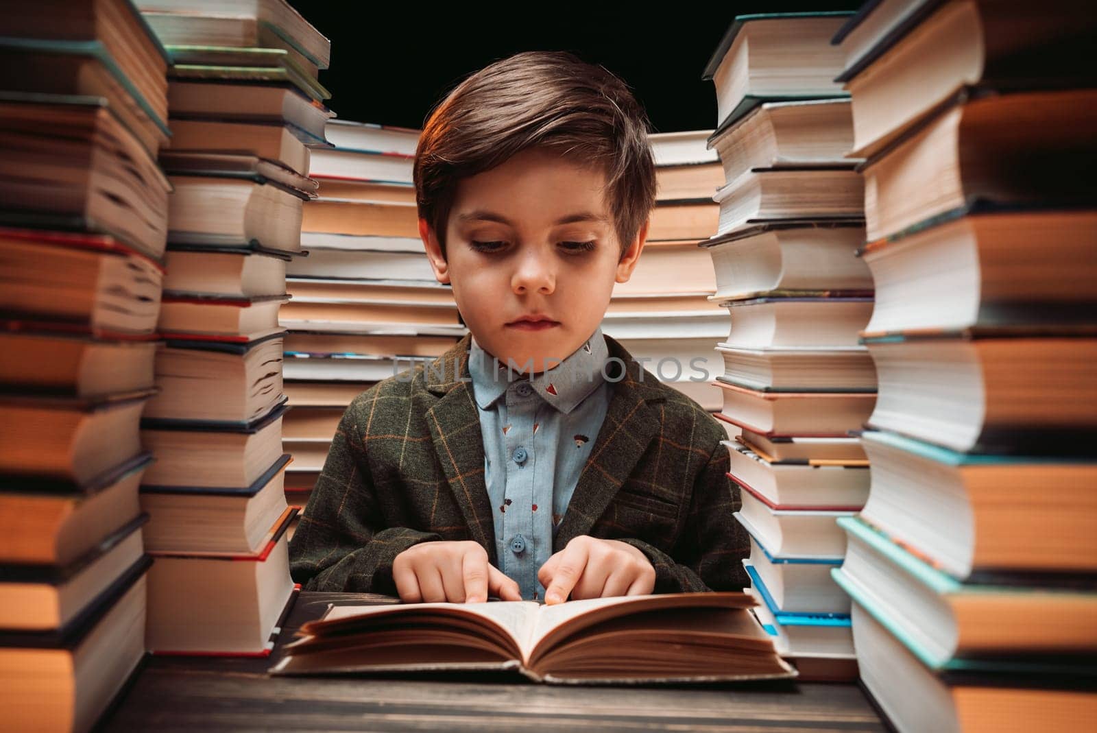Cute little schoolboy reading interesting book in library between stacks of books literature. Education concept, time for kids pleasure. High quality photo