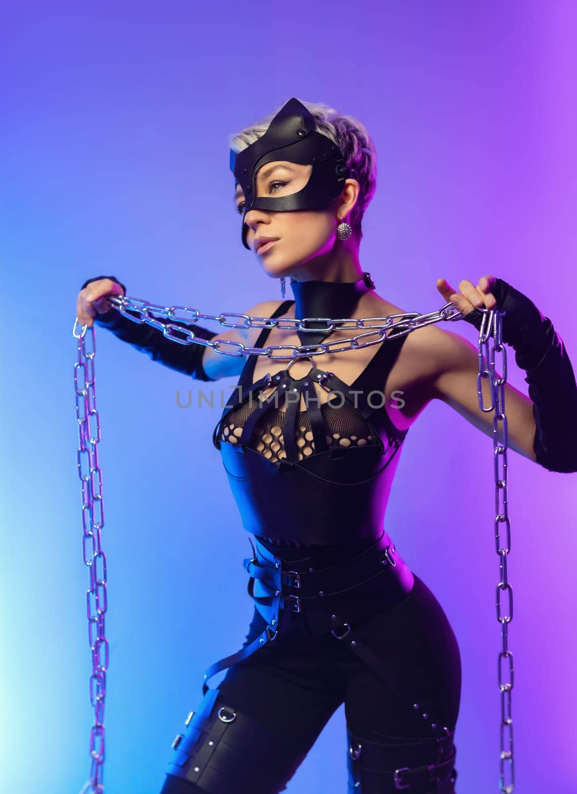 sexy girl in the erotic image of a catwoman in leather belts and a mask poses against the background of a copy paste in a beautiful neon background with a metal chain in her hands by Rotozey