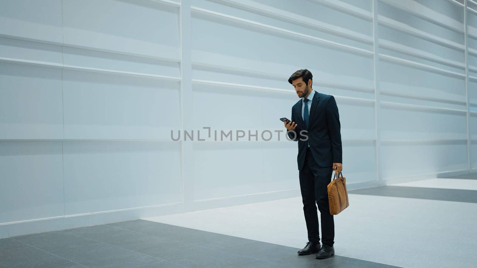 Smart manager looking at phone while standing at white background. Handsome male leader checking email or updated project and planing marketing strategy. while standing at white background. Exultant.