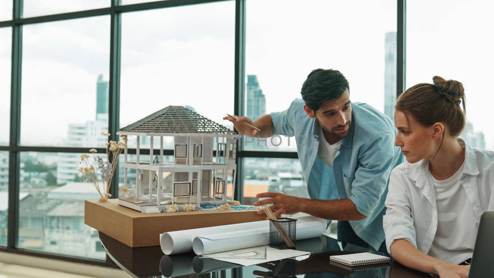 Smart architect engineer inspect house model while colleague using laptop analysis data. Professional designer team working together to design house model construction at modern office. Tracery