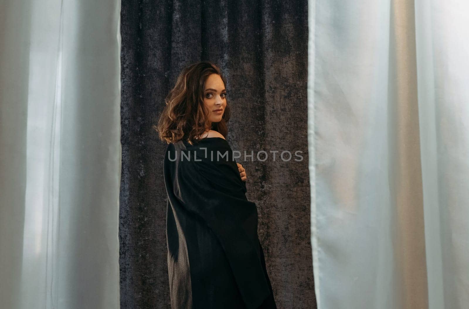 A woman standing in front of a closed curtain, her silhouette visible against the fabric.