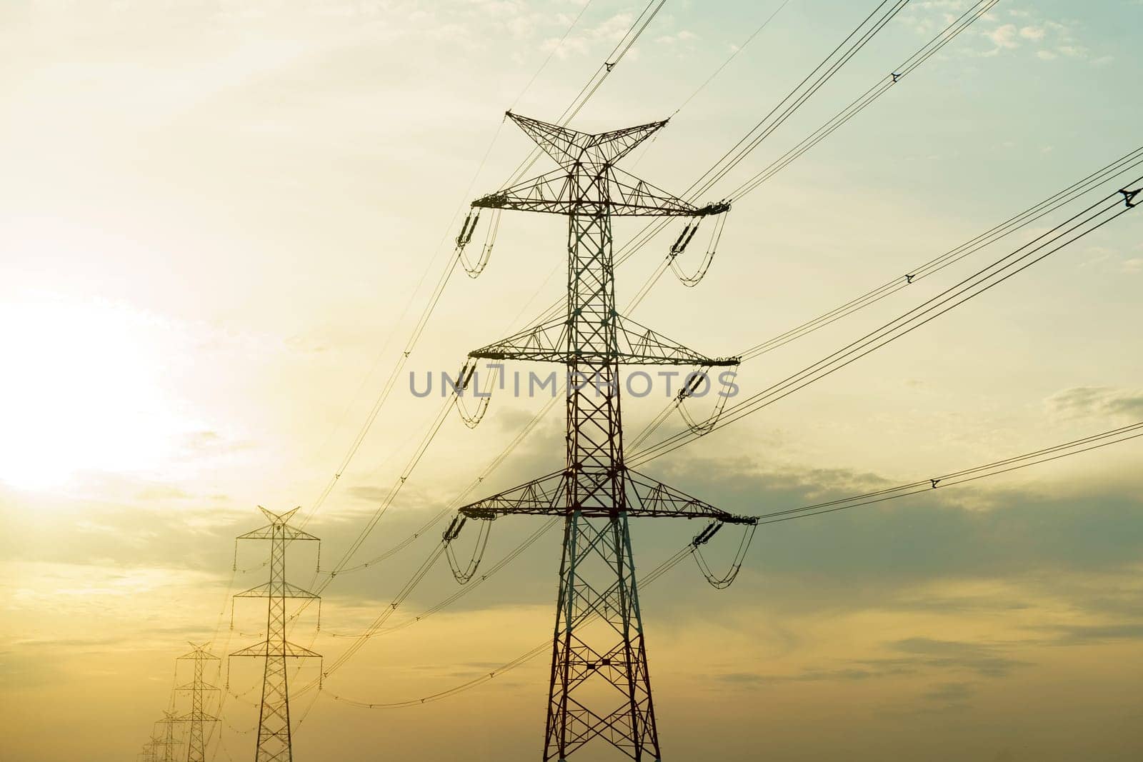 A high voltage power line stands tall against a bright sun in the background, illustrating energy transmission and power distribution infrastructure.