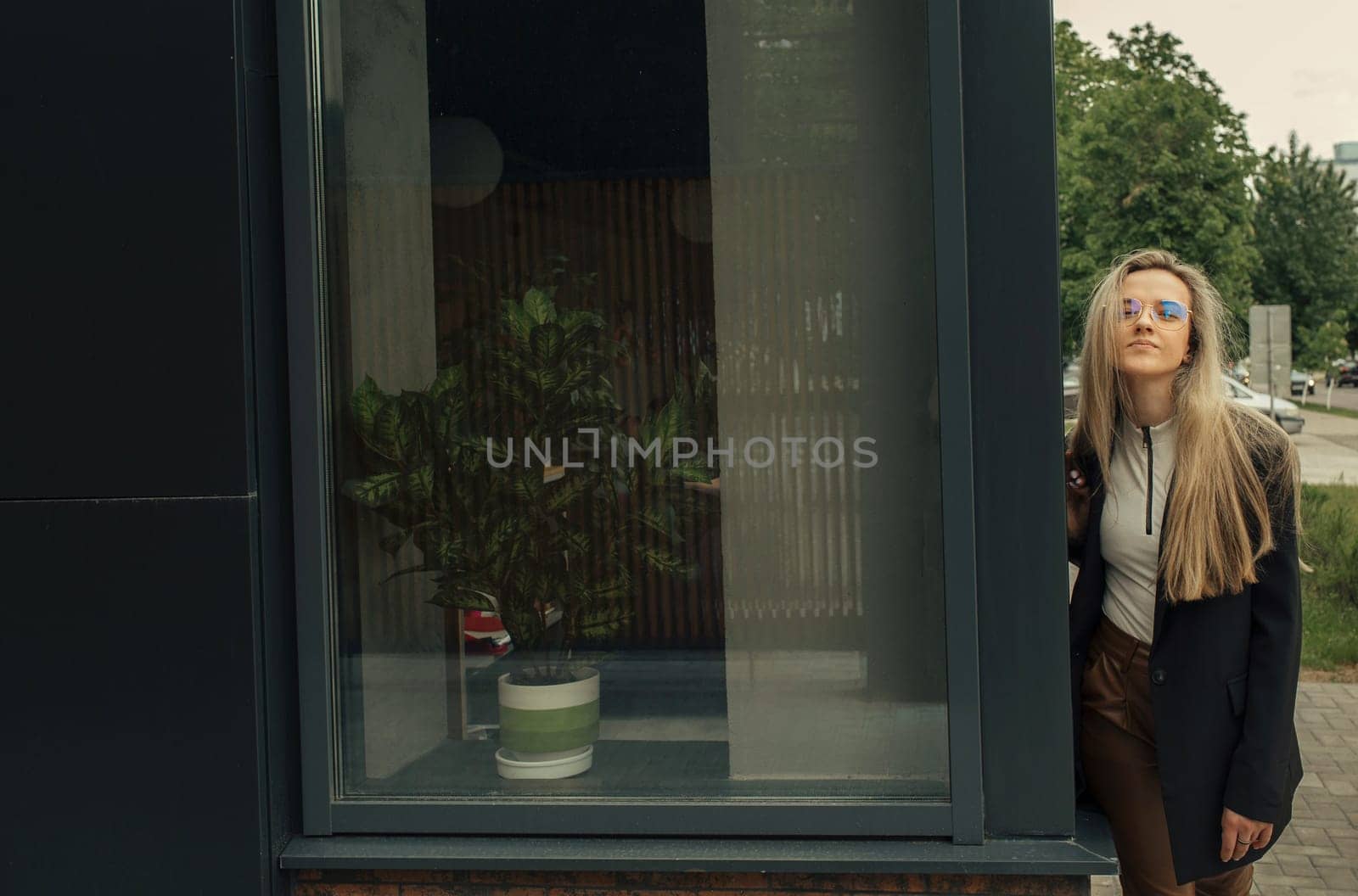 A woman wearing a black jacket is leaning against a glass door outdoors.