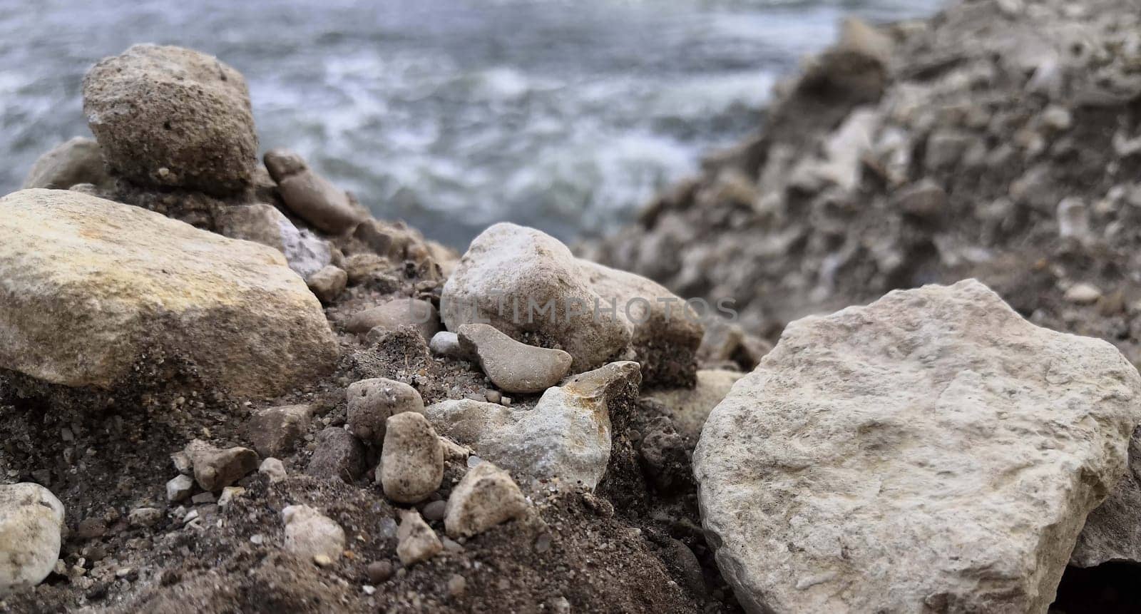 A rock formation stands prominently on the sandy beach, with the vast body of water stretching out in the background. The waves gently crash against the shore under a clear sky.