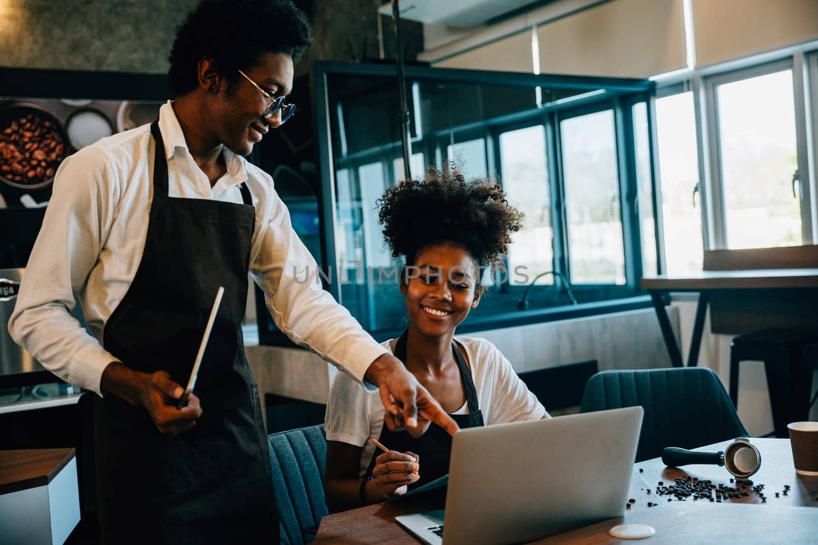 Two cafe owners black barista and owner discuss work on laptop in Coffee Shop. Planning supply orders teamwork business success. Calculating finance discussing menu schedule.