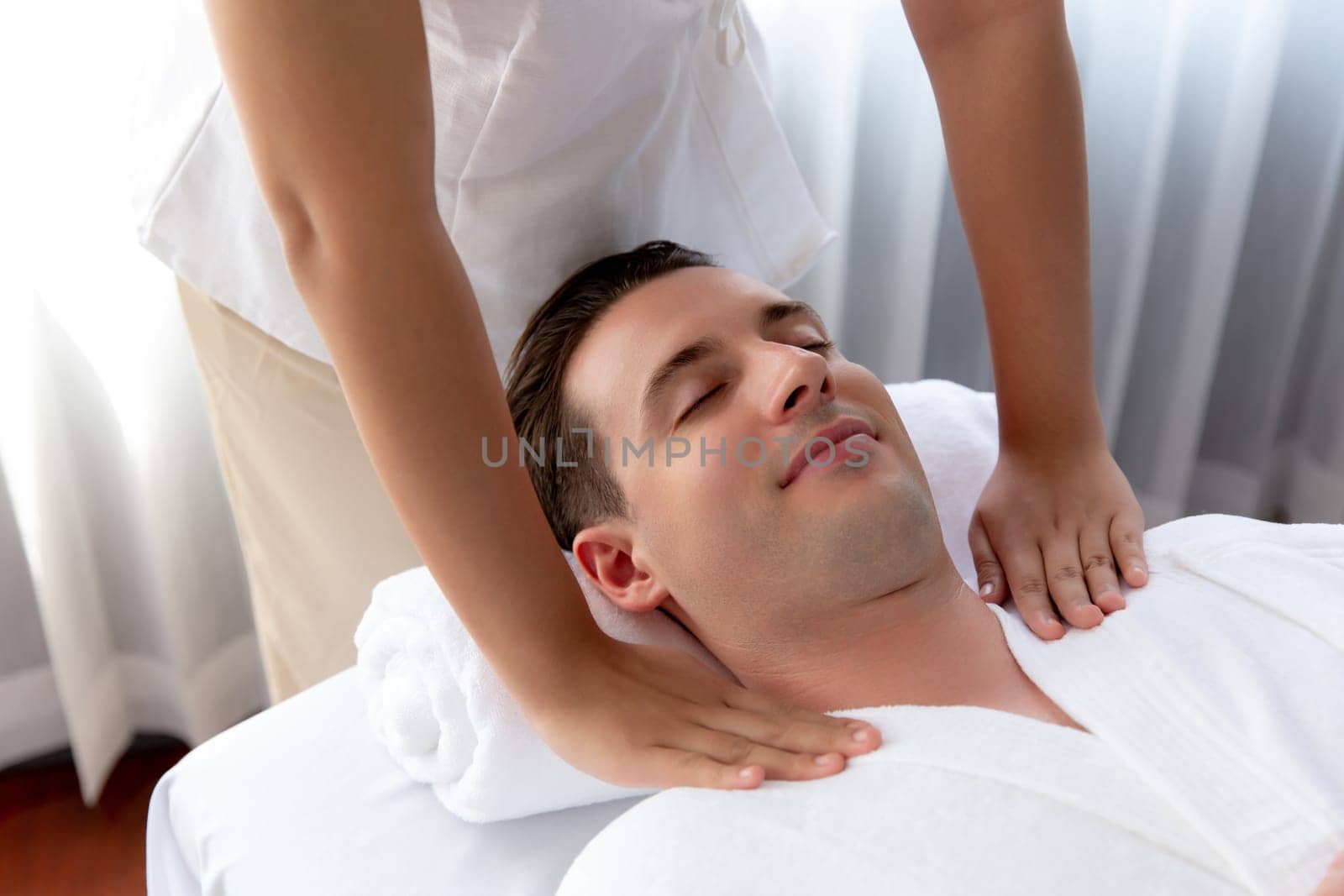 Caucasian man customer enjoying relaxing anti-stress spa massage and pampering with beauty skin recreation leisure in day light ambient salon spa at luxury resort or hotel. Quiescent