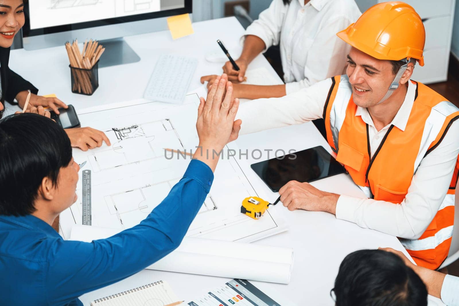 Diverse group of civil engineer and client celebrate and high five after make successful agreement on architectural project, reviewing construction plan and building blueprint at meeting table.Prudent