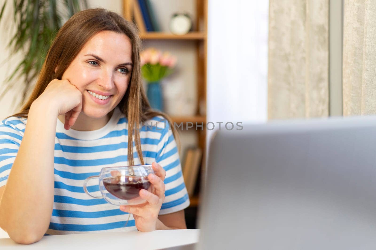 Smiling woman using laptop and holding cup of tea. Casual home office concept with copy space. Design for poster, banner